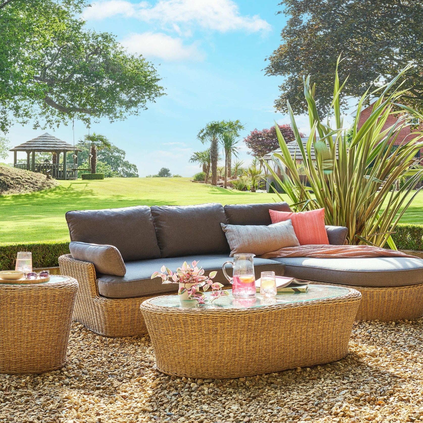 Outdoor patio set with a sofa, ottoman, and coffee table in a garden setting.