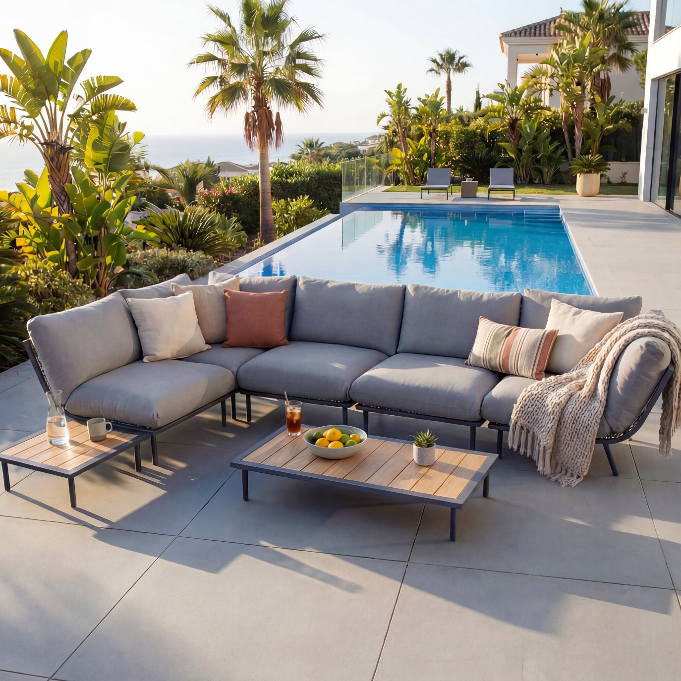 Outdoor patio set with sectional sofa, coffee table, and cushions by a poolside.