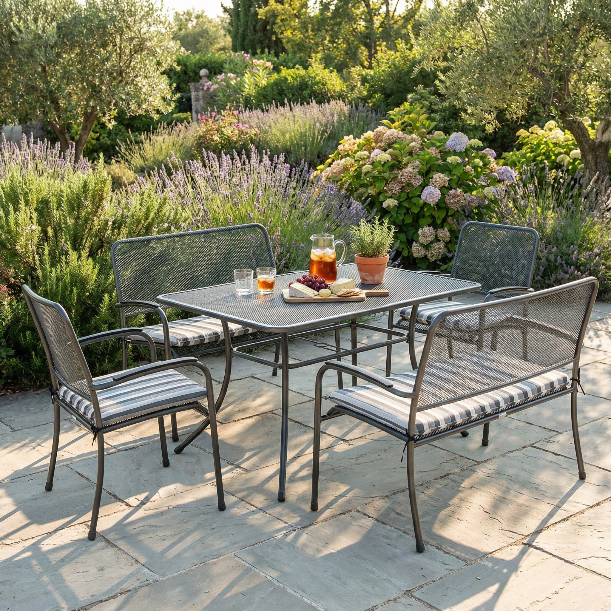 Portofino 4ft garden bench styled as a dining set with matching dining table and armchairs on a patio, with greenery in the background