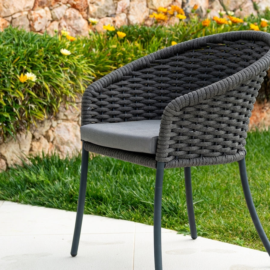 Rope weave chair with a cushion on a patio area with greenery and flowers in the background