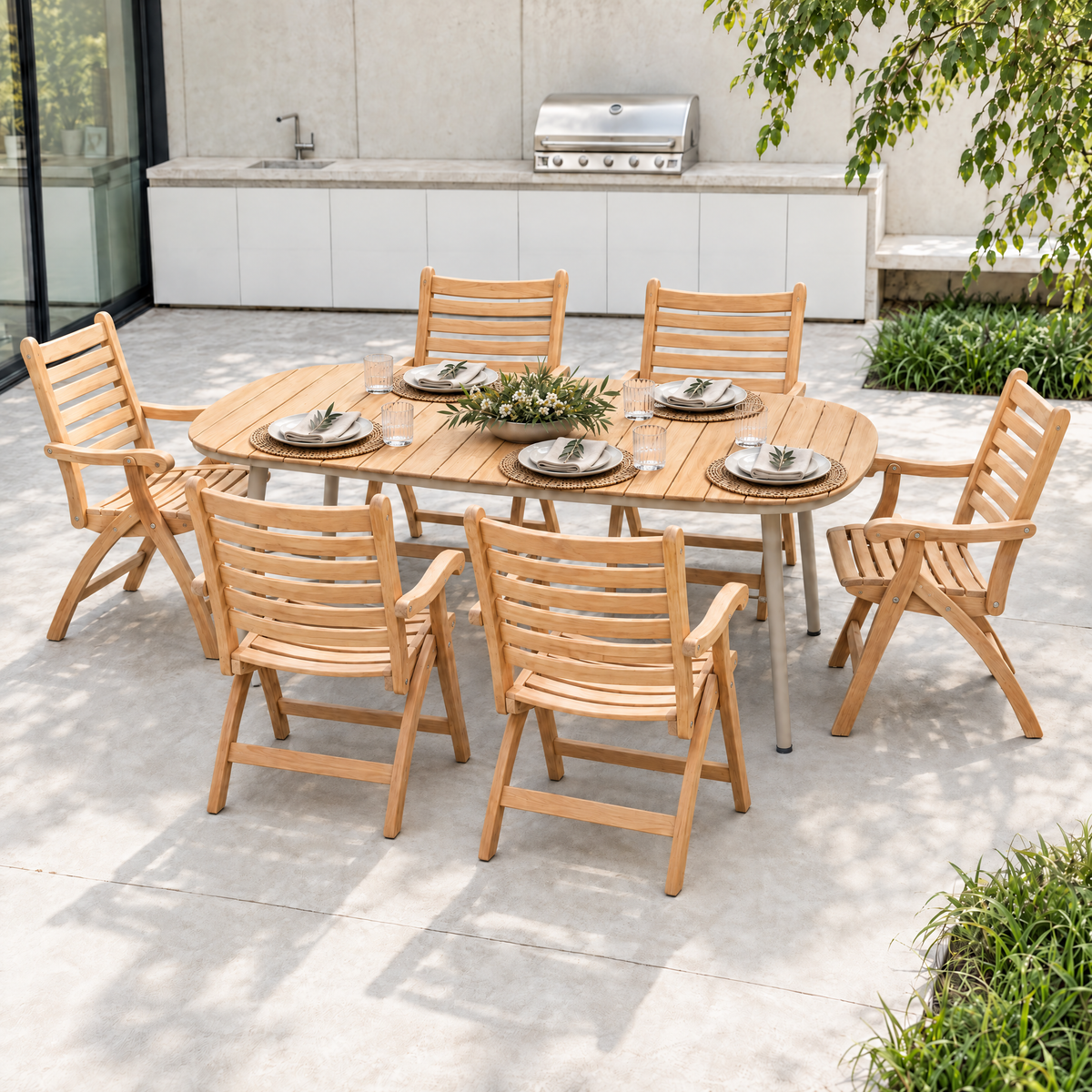 An outdoor dining set consisting of a rectangular teak wood table and six matching slatted armchairs, arranged on a concrete patio in a backyard setting with a grill and greenery in the background.