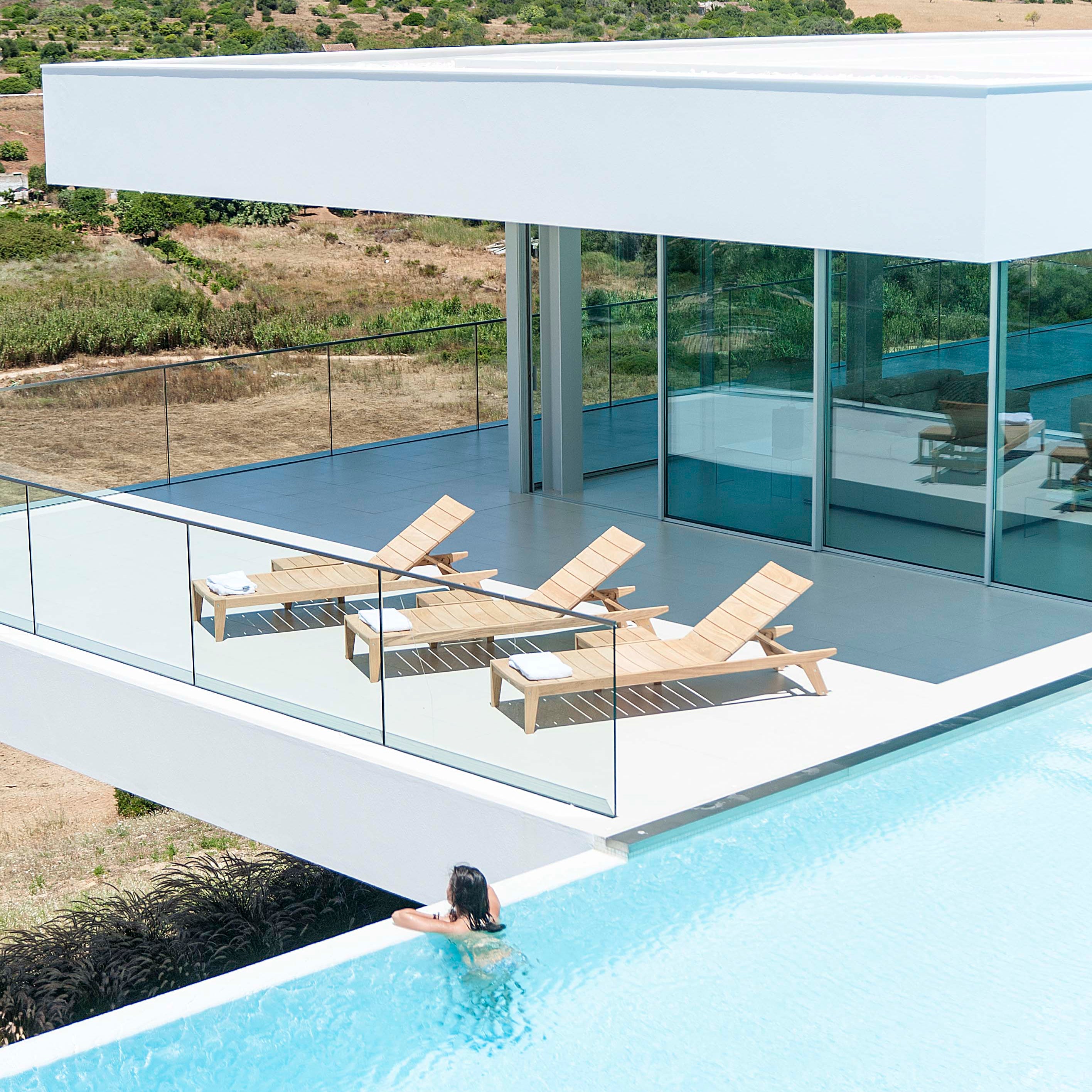overhead view of 3 roble sun loungers on a patio area with a white building in the background an a pool in the foreground