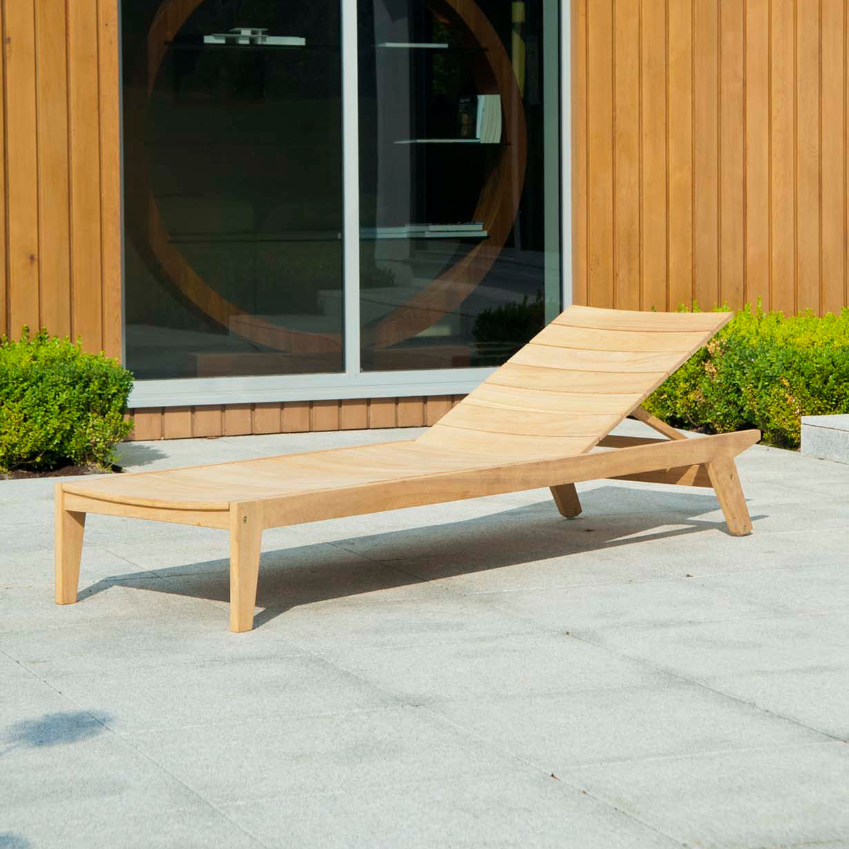wood sun lounger on a patio in front of a garden room