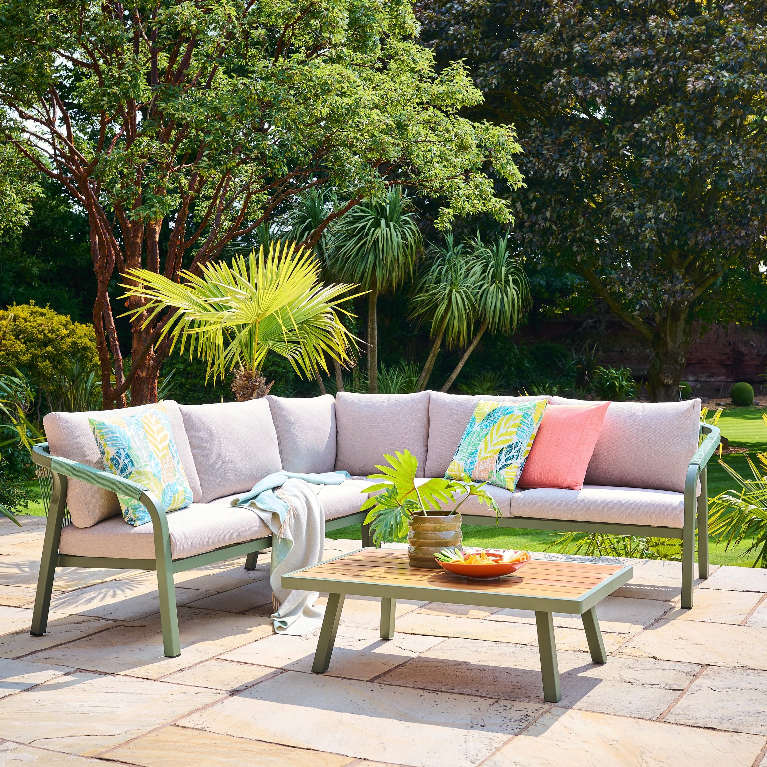Outdoor patio set with a sectional sofa and coffee table in a garden setting.