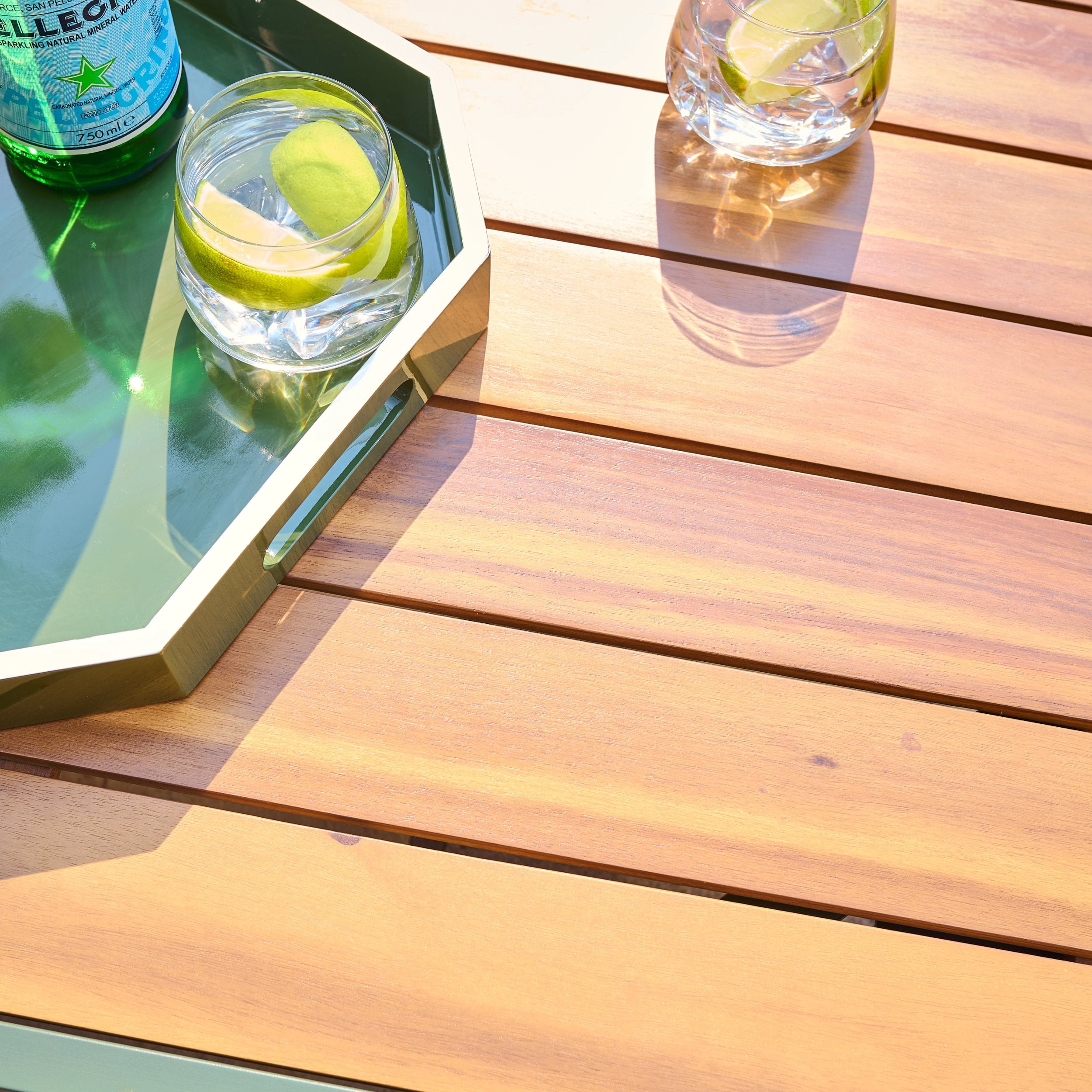 Two glasses of water with lime wedges on a wooden table, accompanied by water
