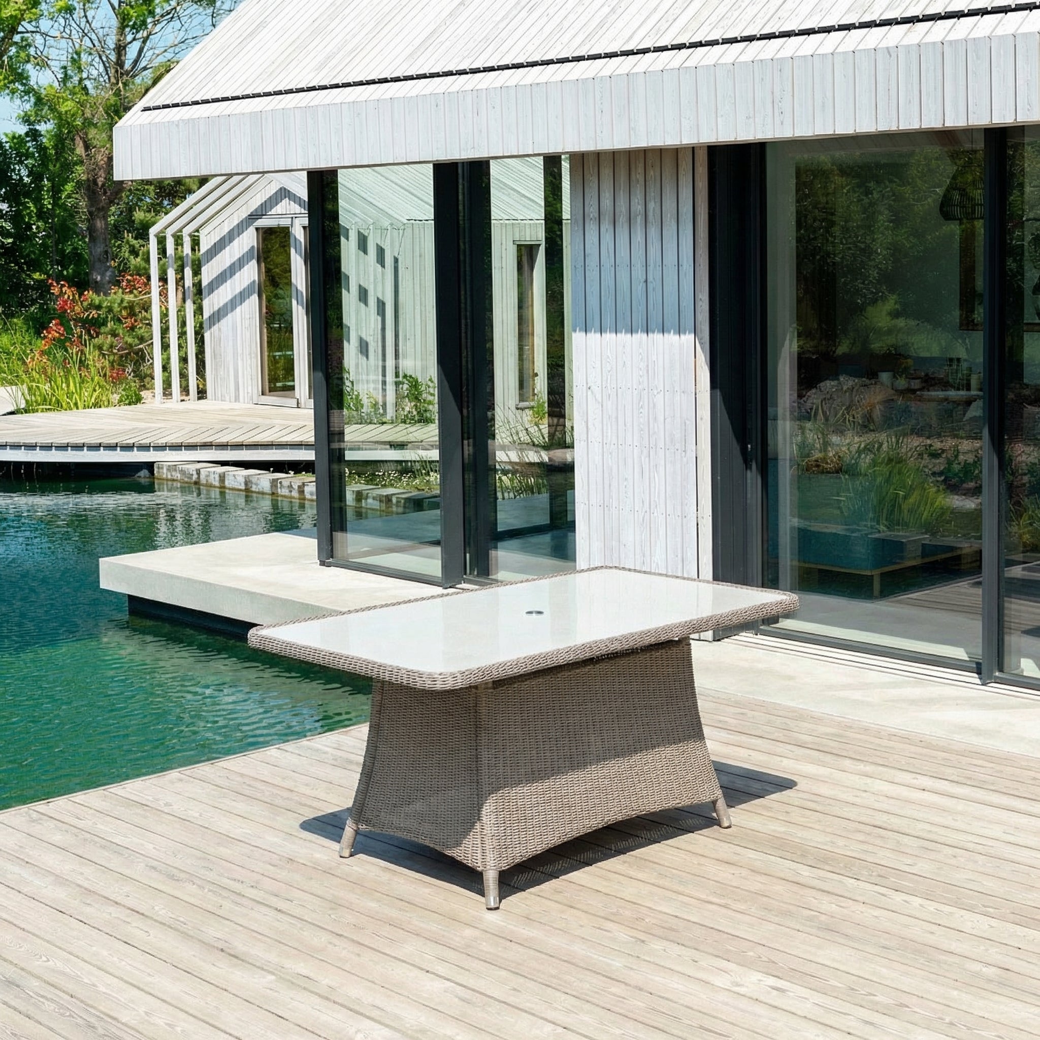 Outdoor furniture set on a wooden deck by a pool with a modern house in the background
