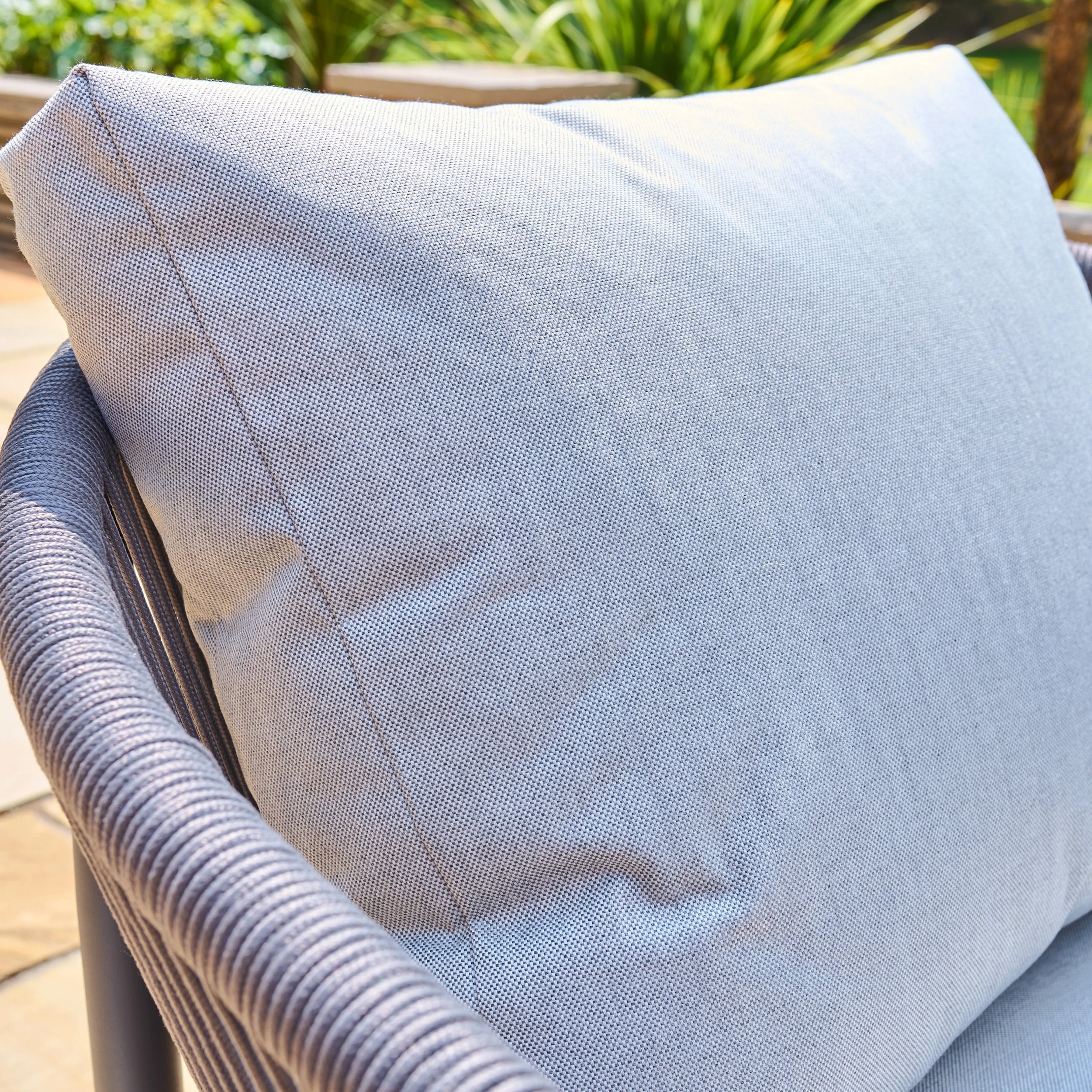 Grey cushion on a rope weave chair with a blurred natural background