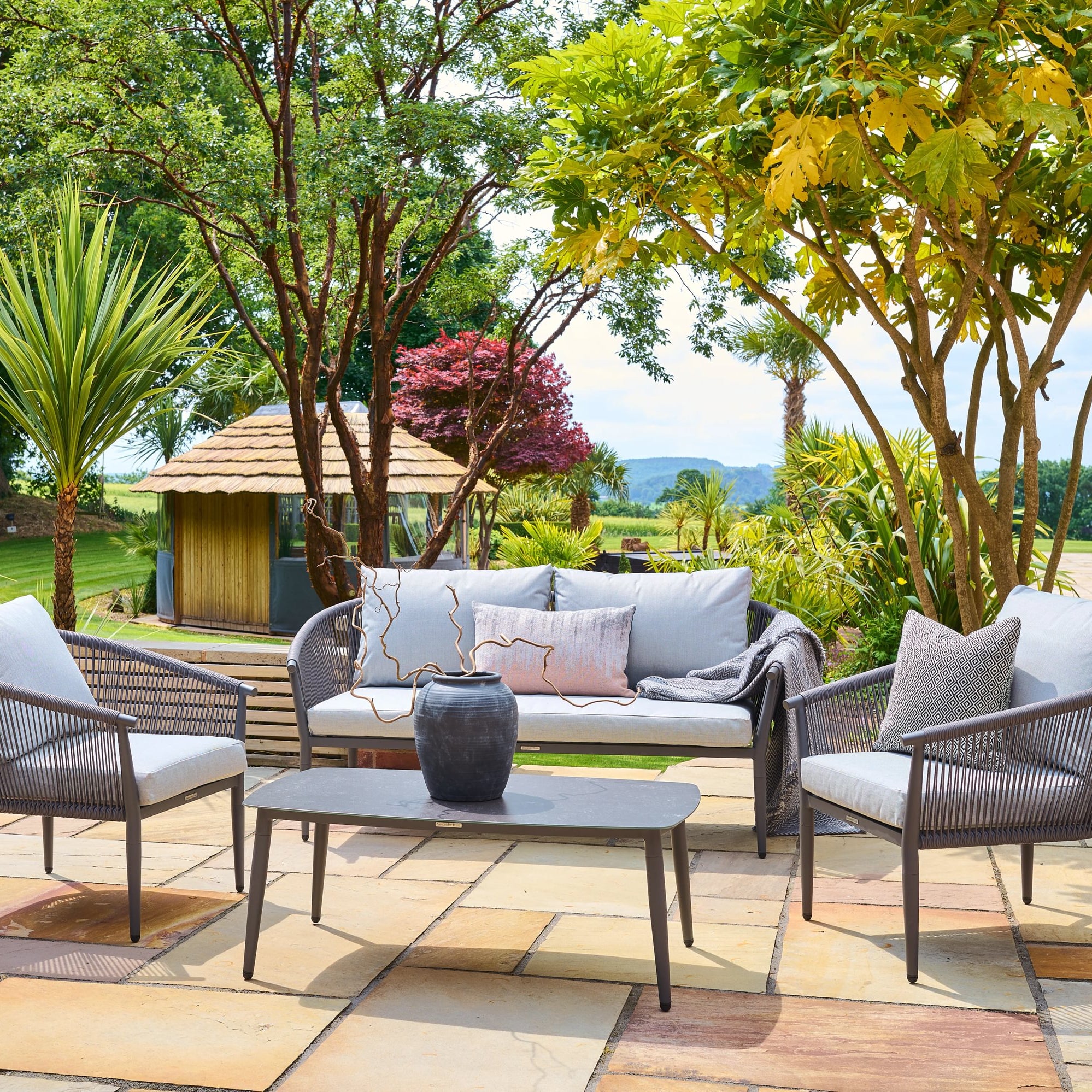 Kyoto outdoor patio set with chairs, table, and sofa on a stone patio with trees and garden in the background.