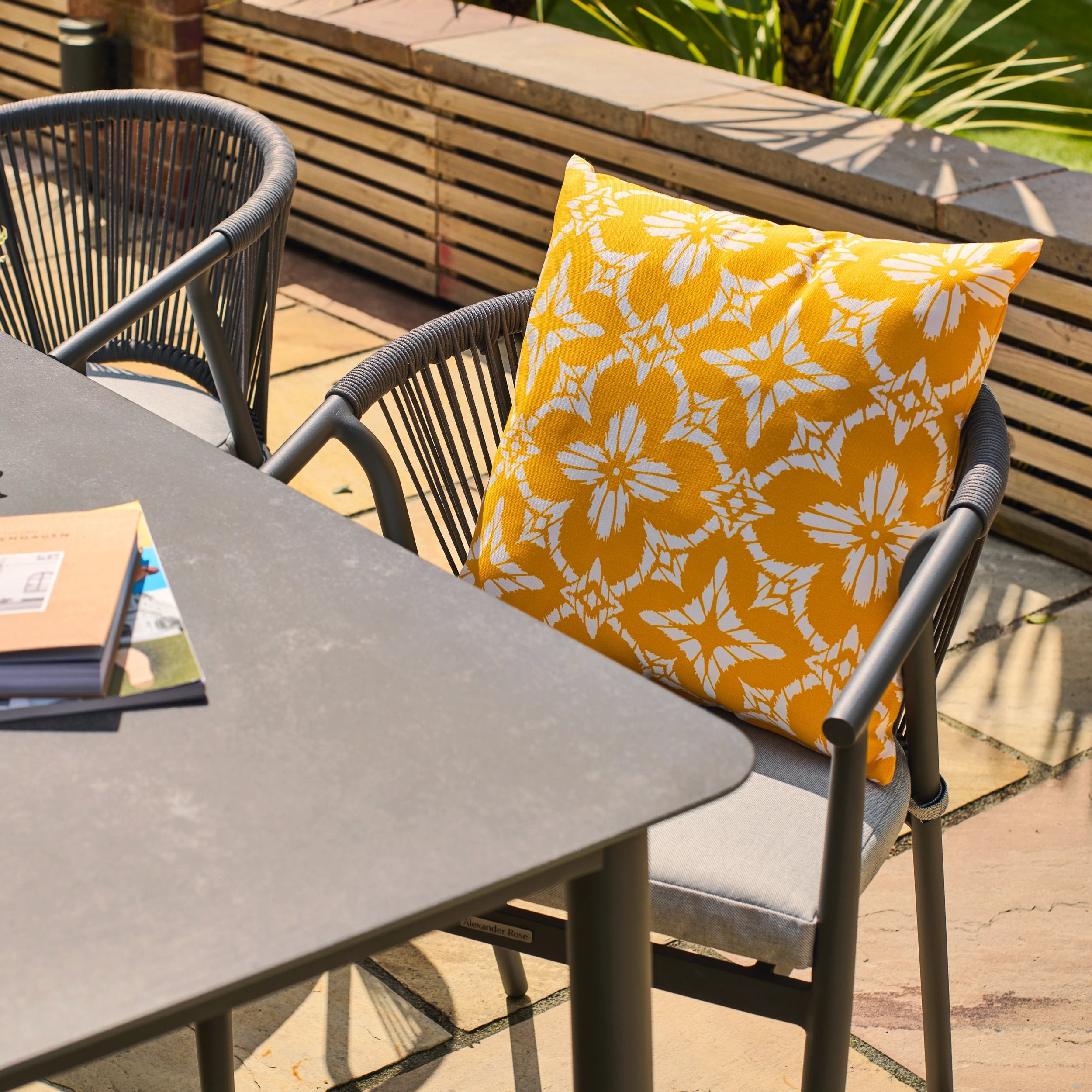 Outdoor setting with a chair featuring a yellow floral outdoor cushion and a table.