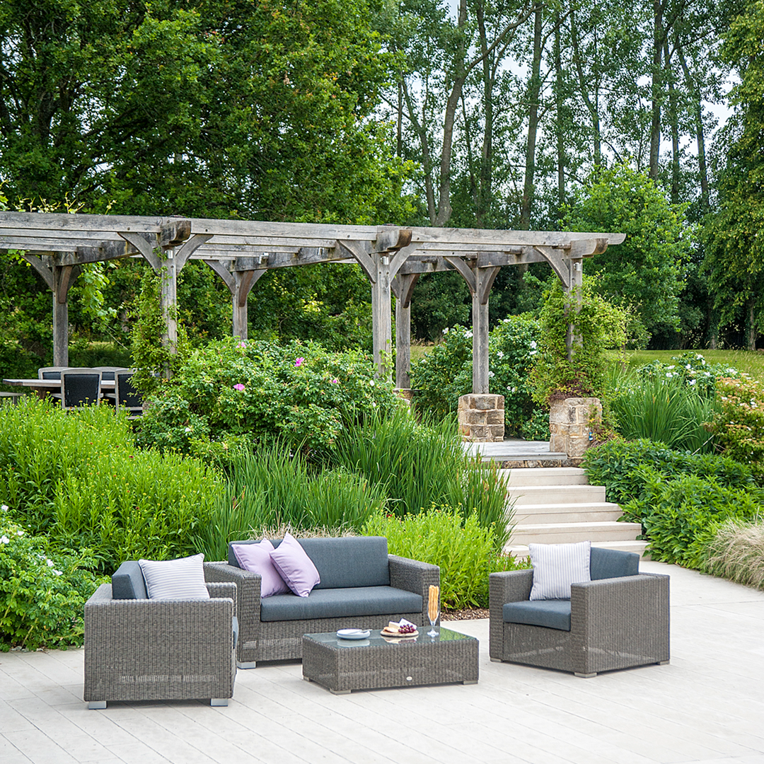 Outdoor patio set, sofa, two chairs and a coffee table with grey cushions in a garden setting