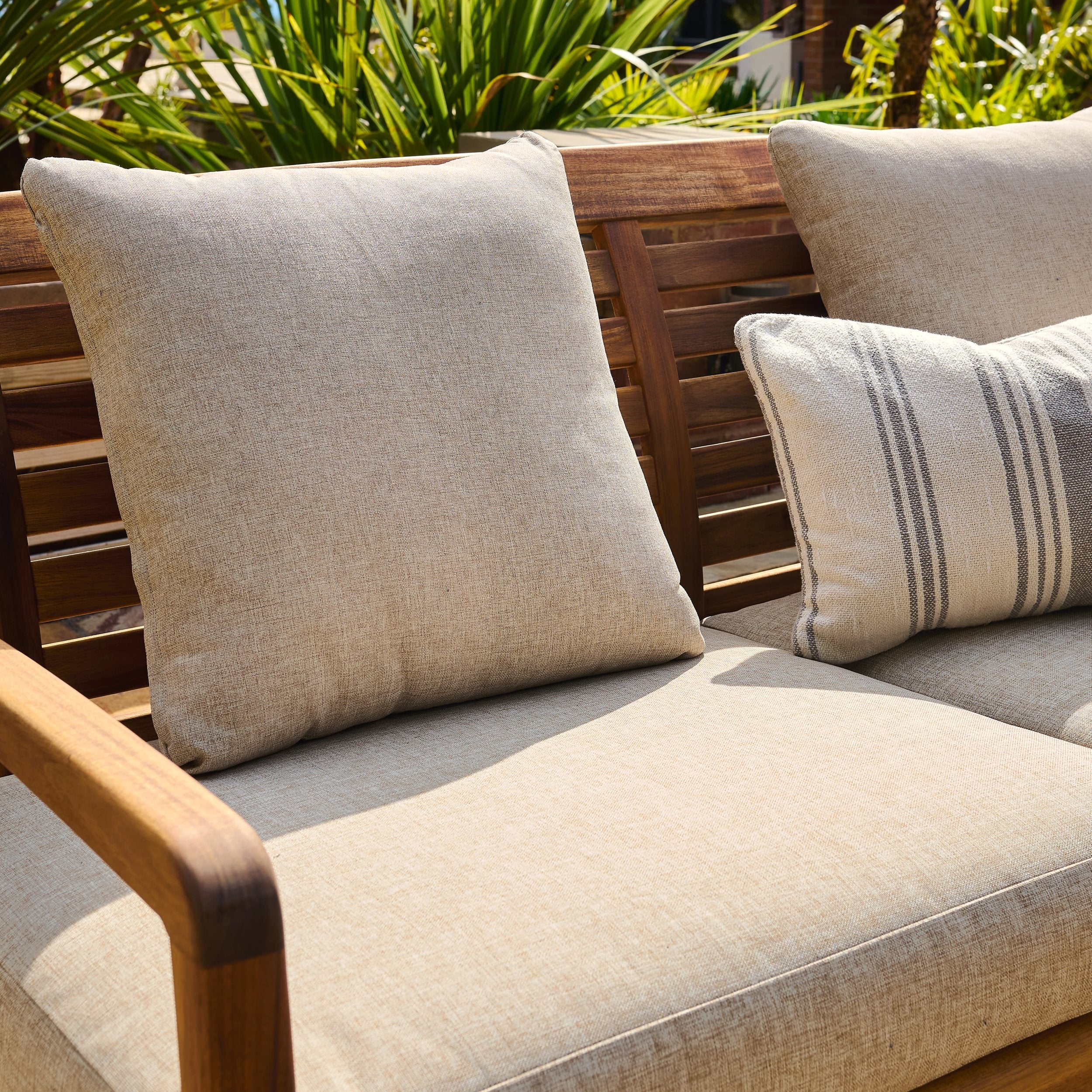 Beige outdoor cushions on a wooden bench with greenery in the background