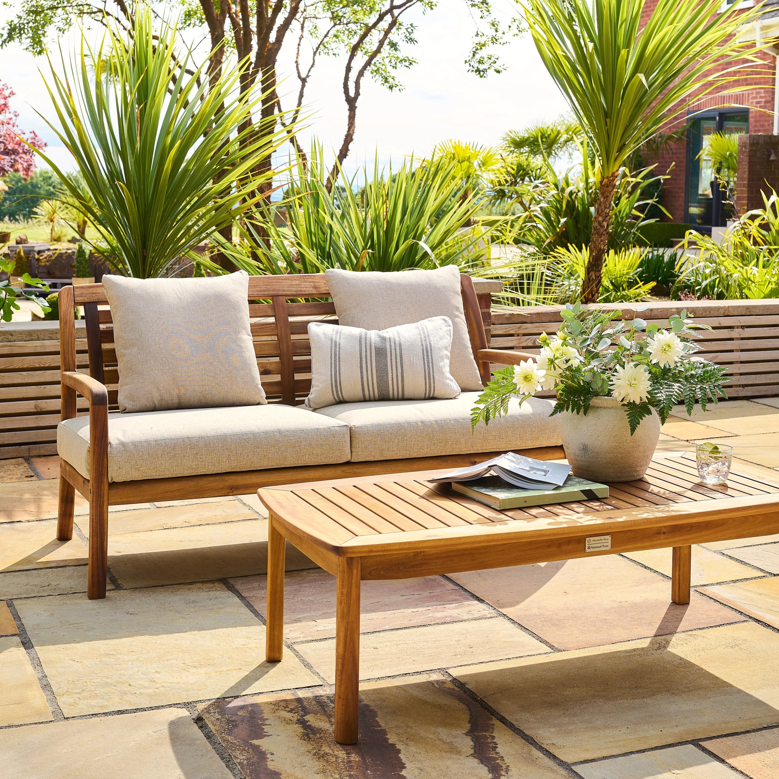 Wooden outdoor sofa with cushions and a coffee table with a plant on a patio