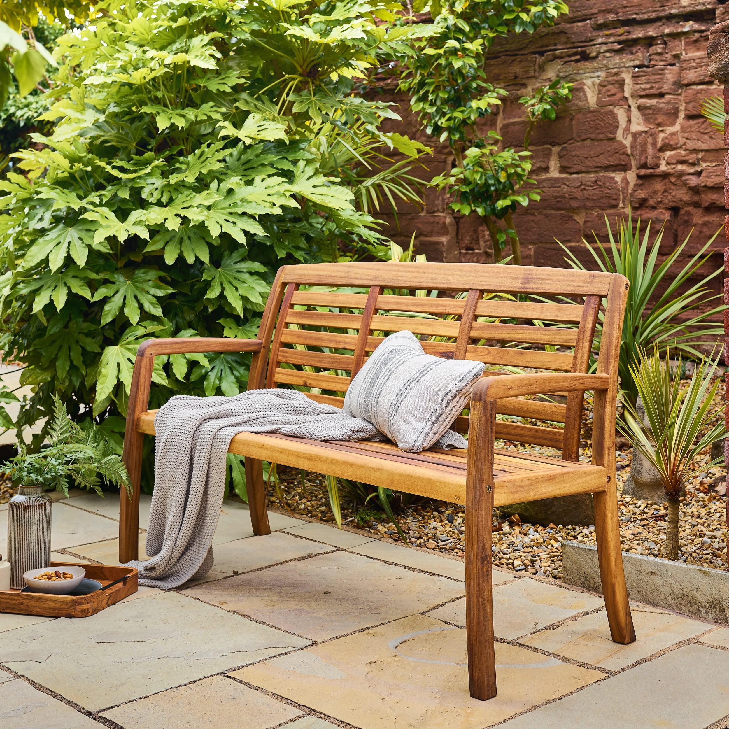 Wooden bench with a blanket and pillow in a garden setting