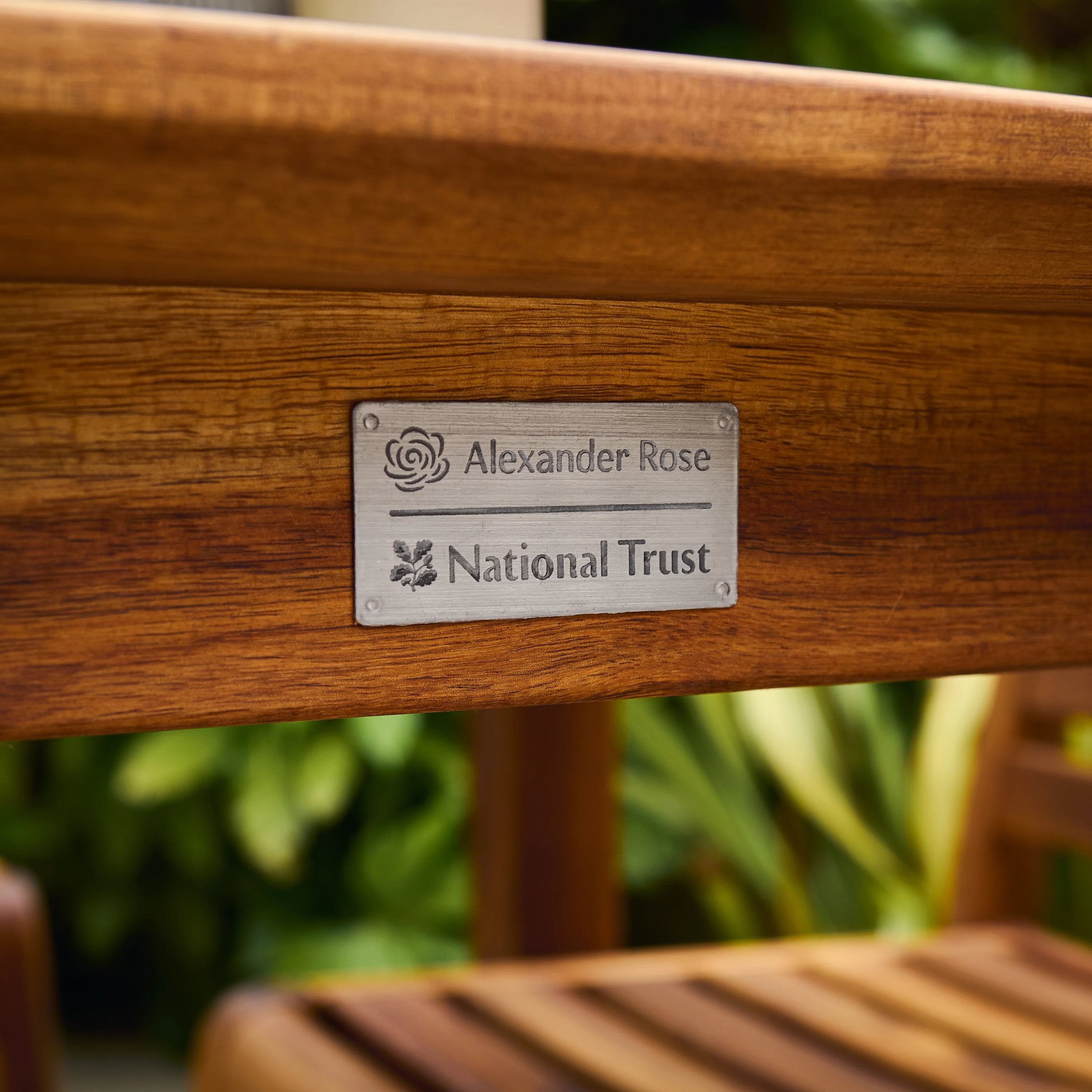 Wooden bench with 'Alexander Rose National Trust' plaque against a blurred green background