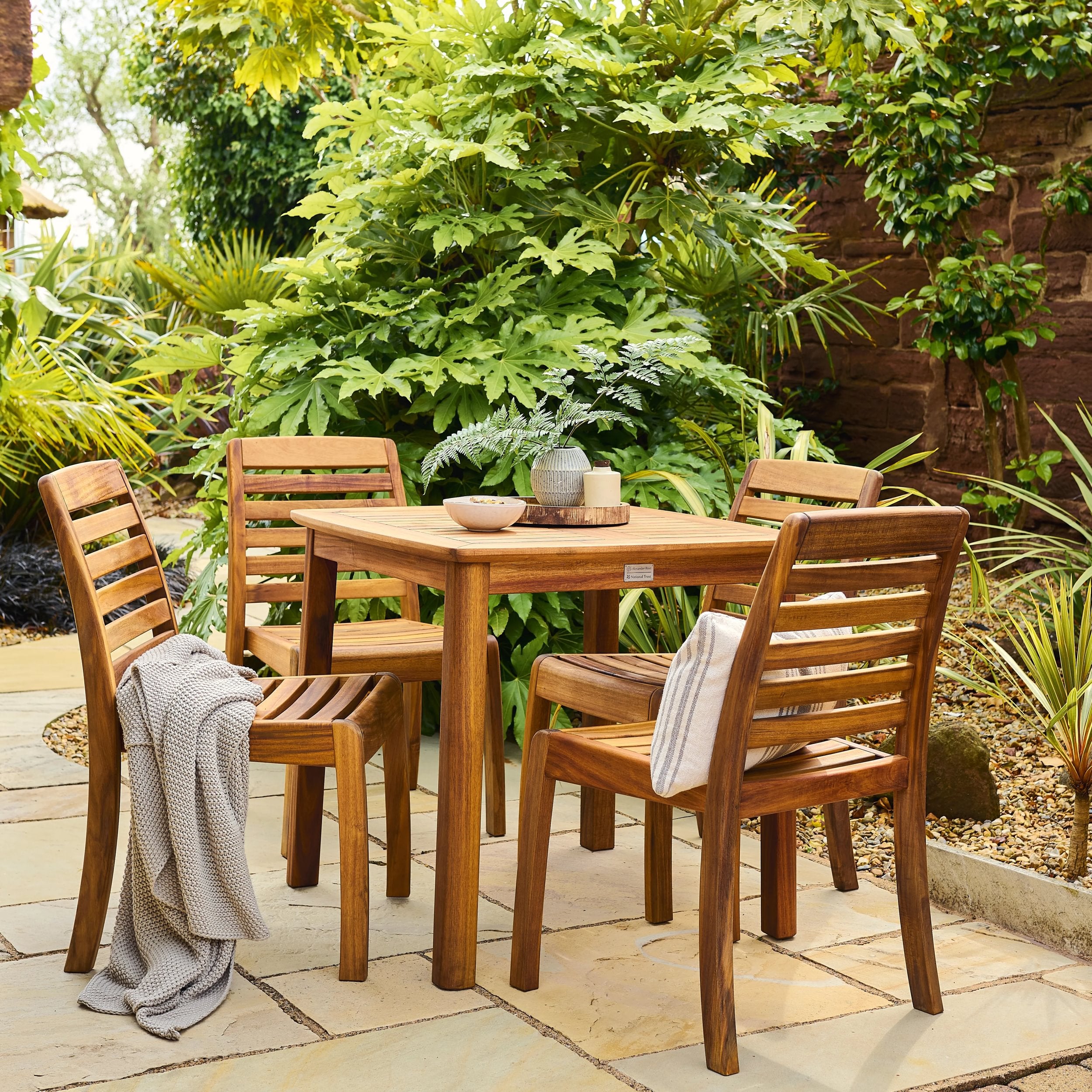 Wooden outdoor dining set with table and chairs on a patio surrounded by greenery.