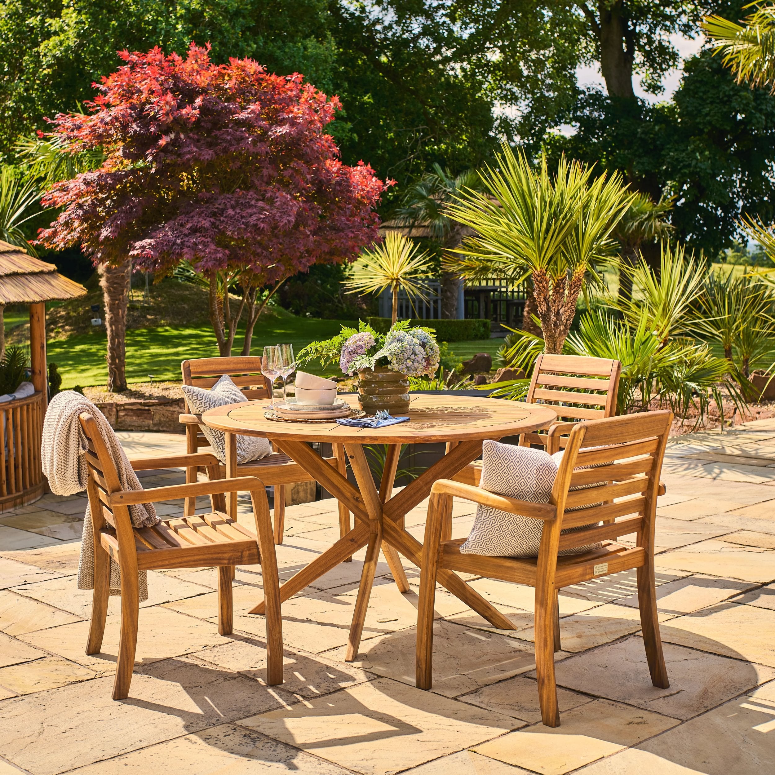 Wooden outdoor dining set with table and chairs on a patio, surrounded by greenery.