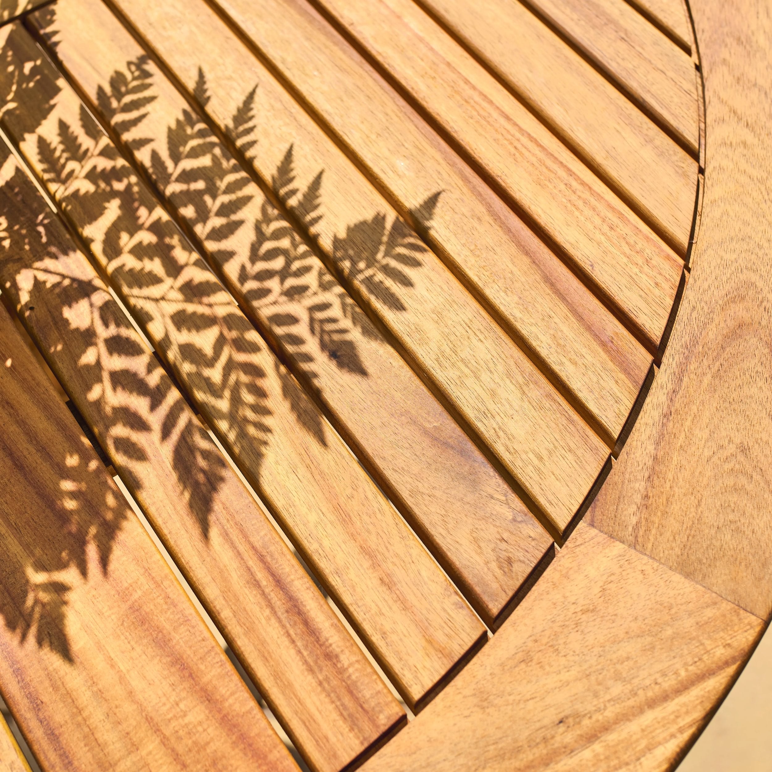 Wooden table top with a fern shadow cast on it