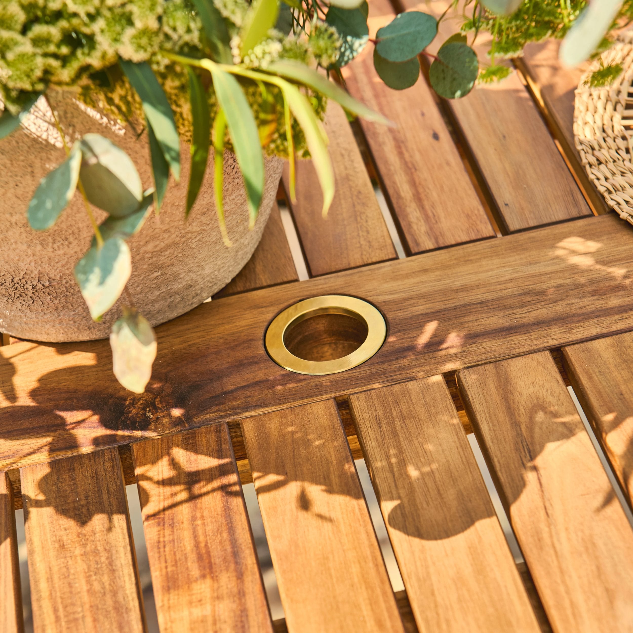 Wooden table with a gold umbrella hole and greenery on a wooden surface