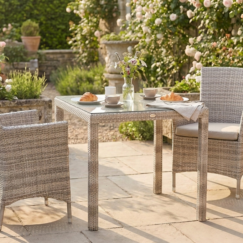 Outdoor patio set with table and chairs surrounded by flowers and plants.