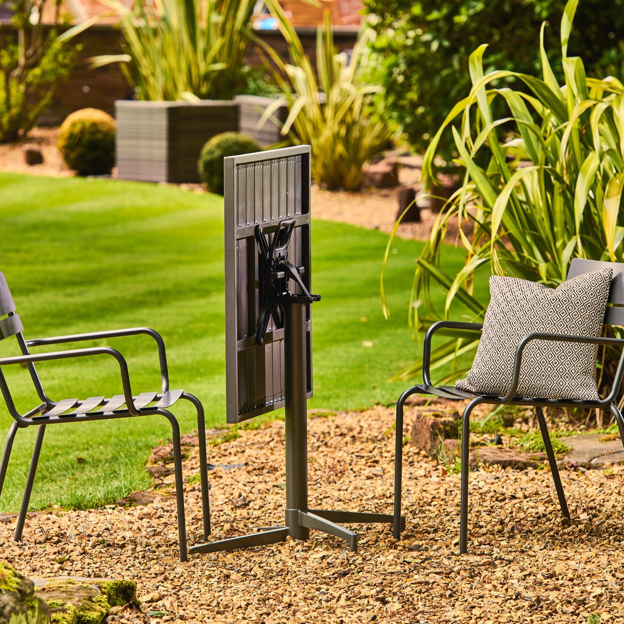 Garden scene with two chairs and a folding table in a garden setting.