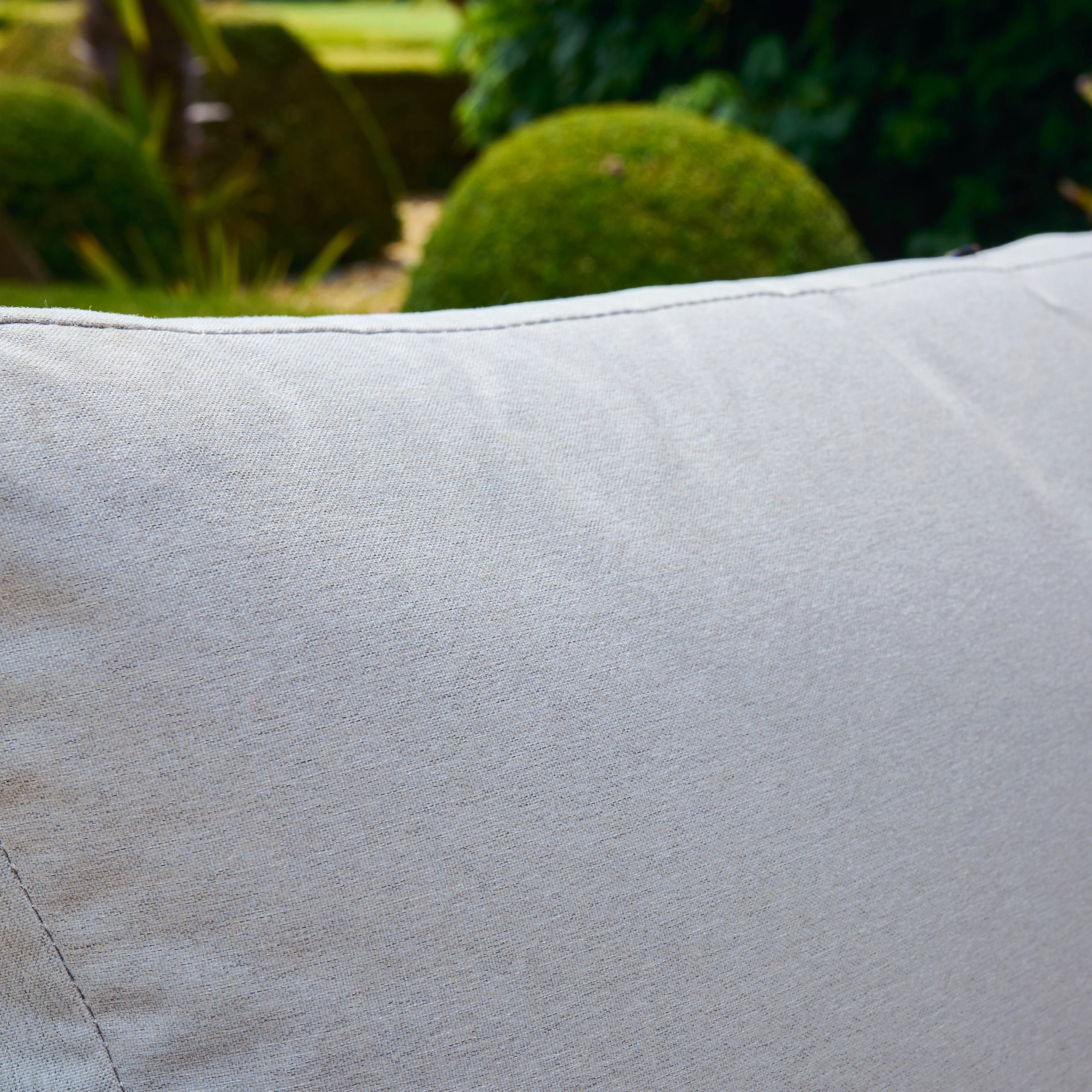 Close-up of a light gray cushion with a blurred green garden background