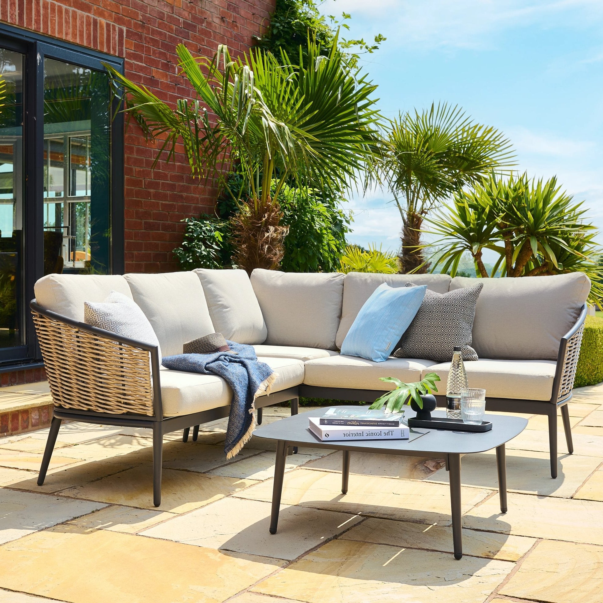 Outdoor patio set with sectional sofa, coffee table, and cushions on a stone patio.