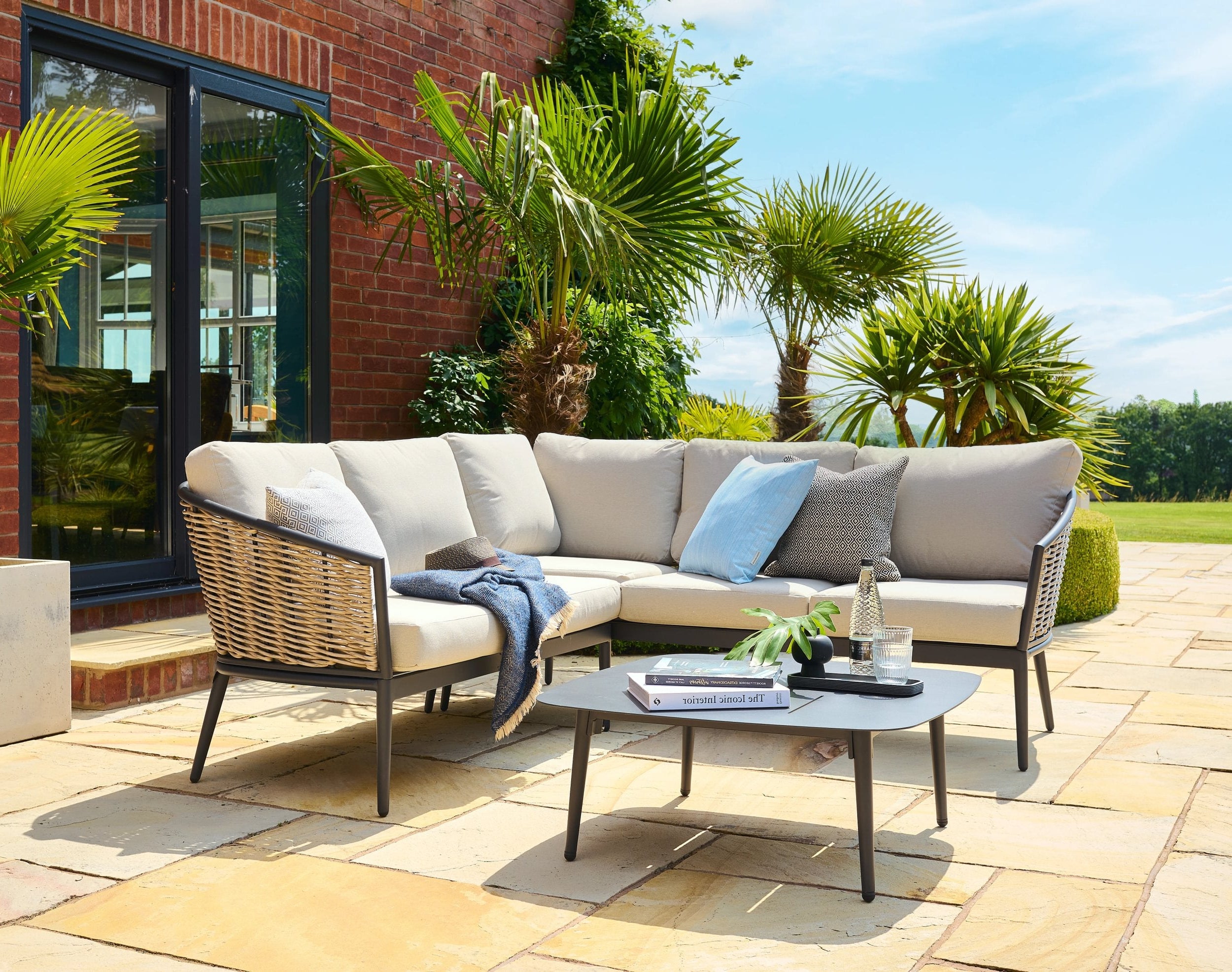 Outdoor patio set with sectional sofa, coffee table, and cushions on a stone patio.