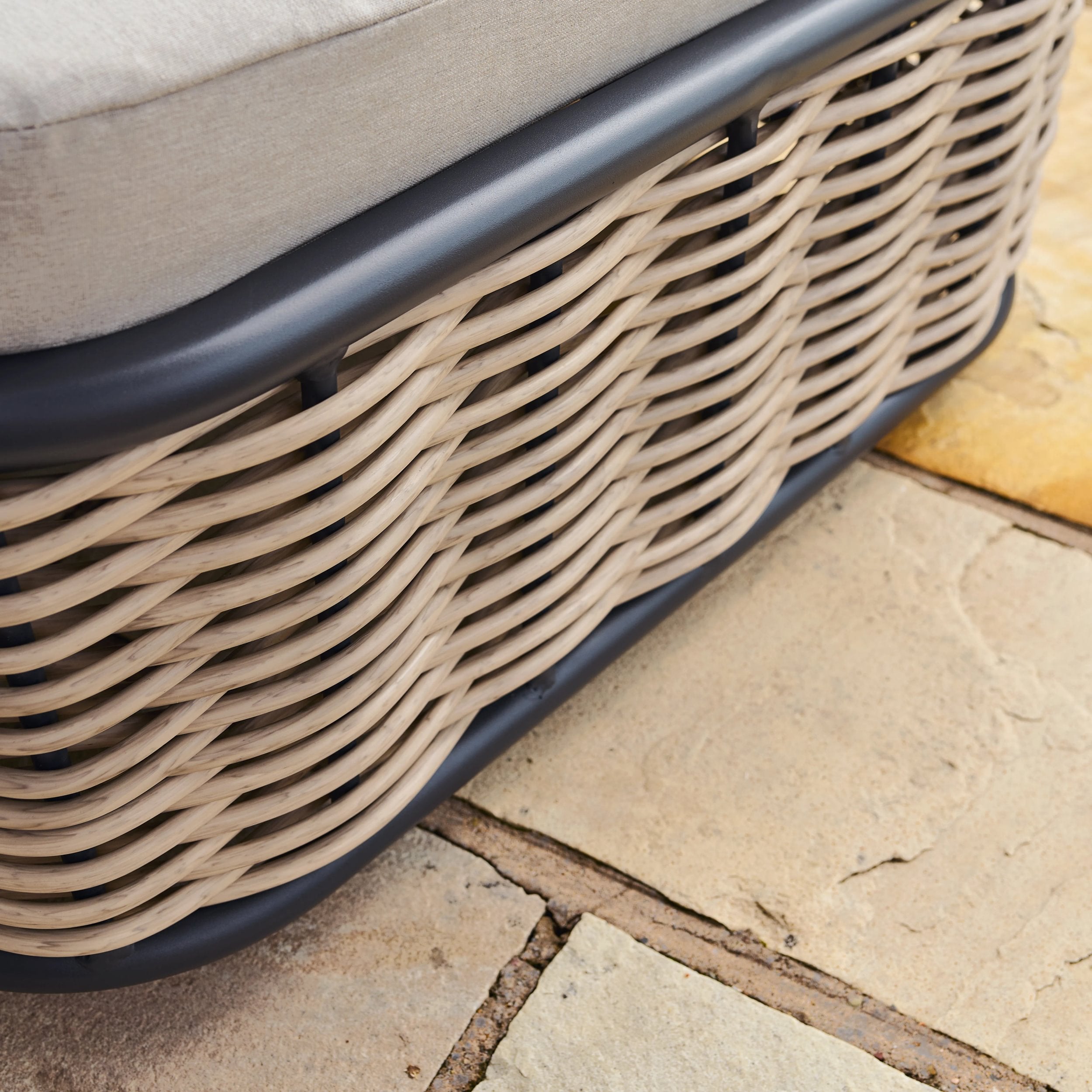 Close-up of a rattan sun lounger with a cushion on a stone patio