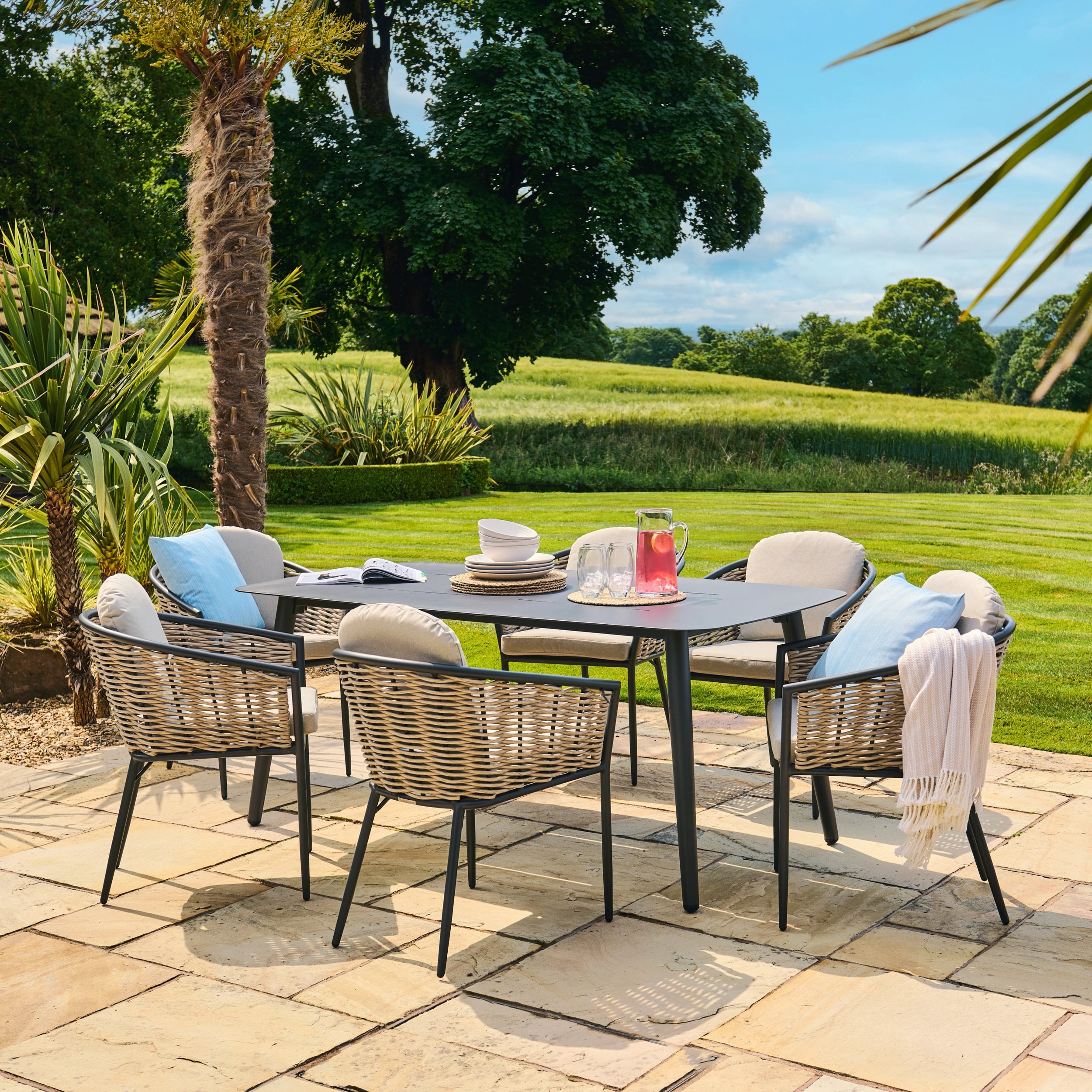 Outdoor dining set with chairs and table on a patio area with greenery in the background