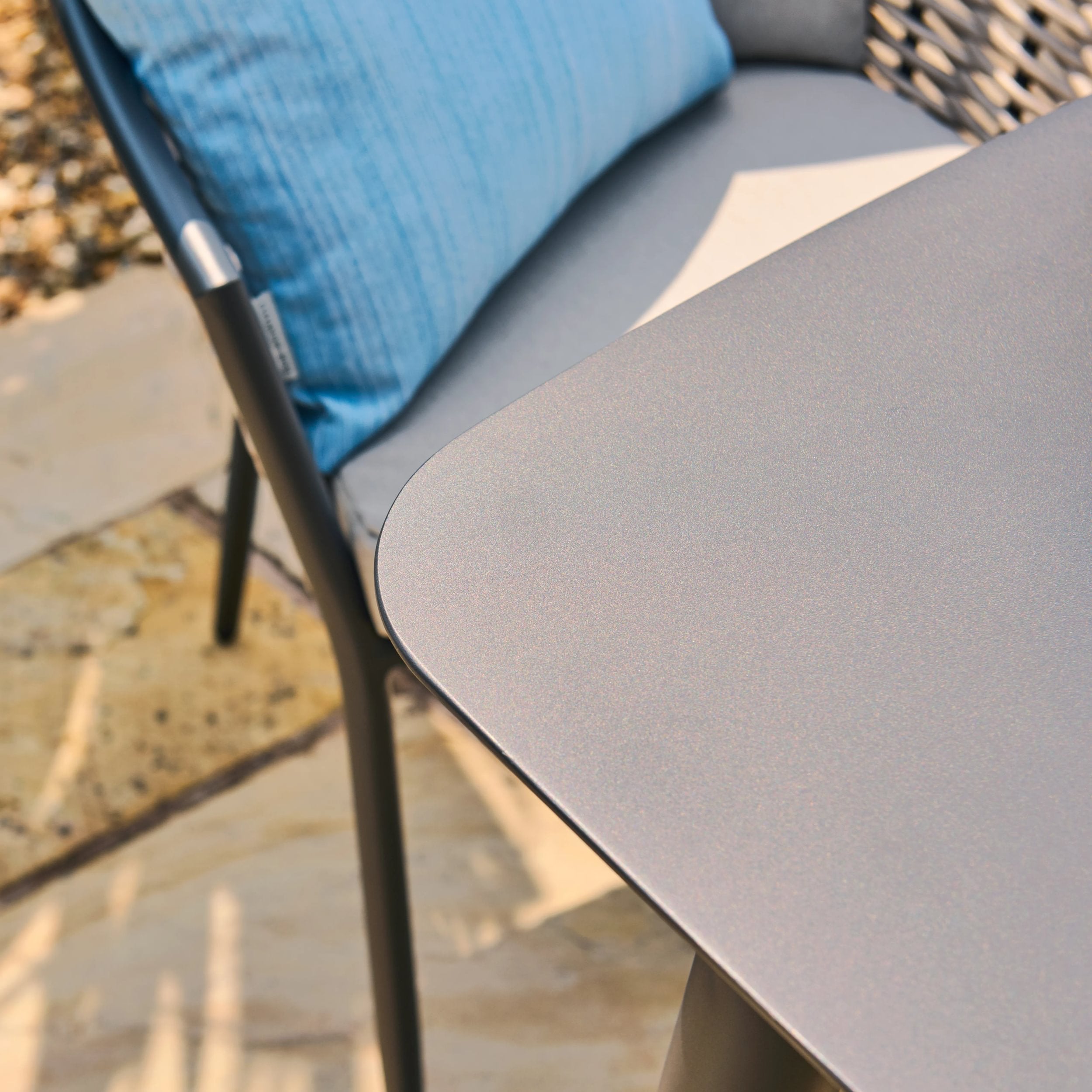 Gray chair with a blue cushion on a stone patio