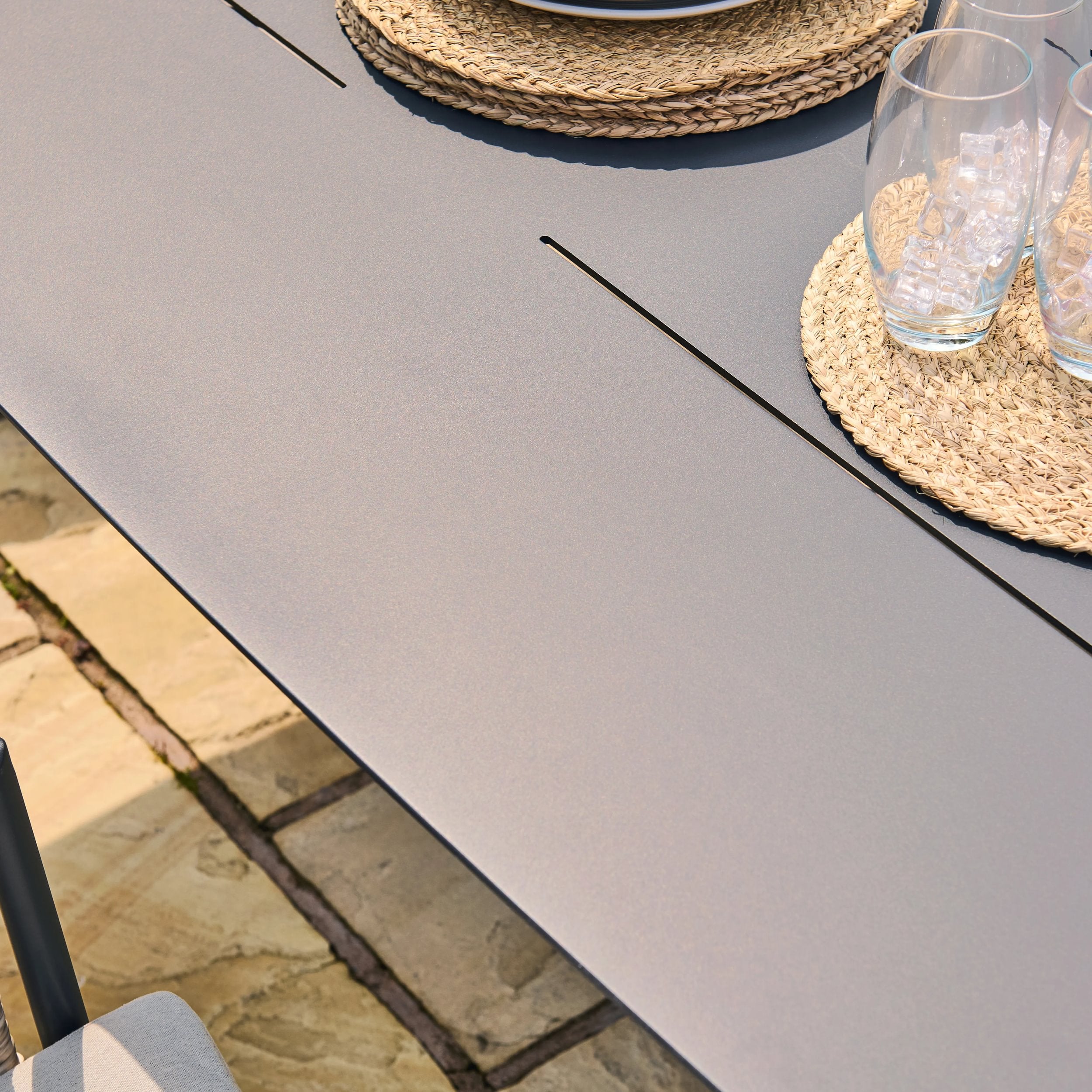 Gray outdoor dining table with glasses and placemats on a stone patio