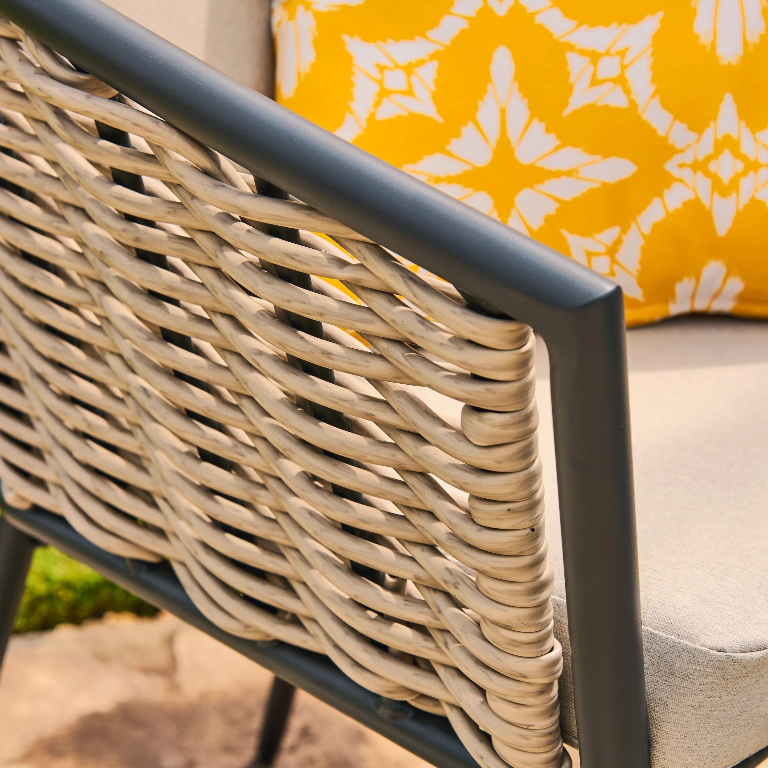 Close-up of a rattan chair with a yellow cushion featuring a white floral pattern.