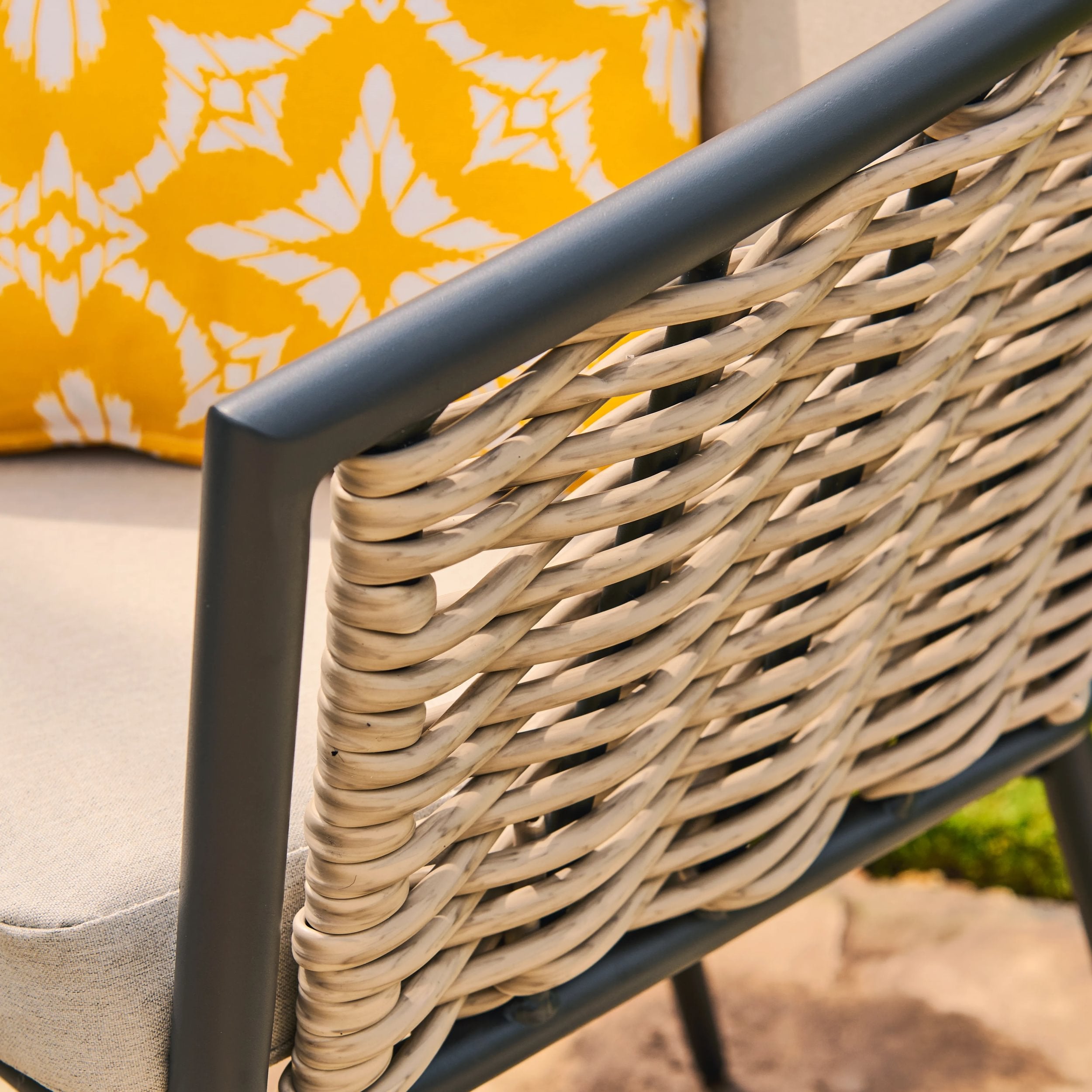 Close-up of a rattan and metal chair with a yellow cushion featuring a white floral pattern.