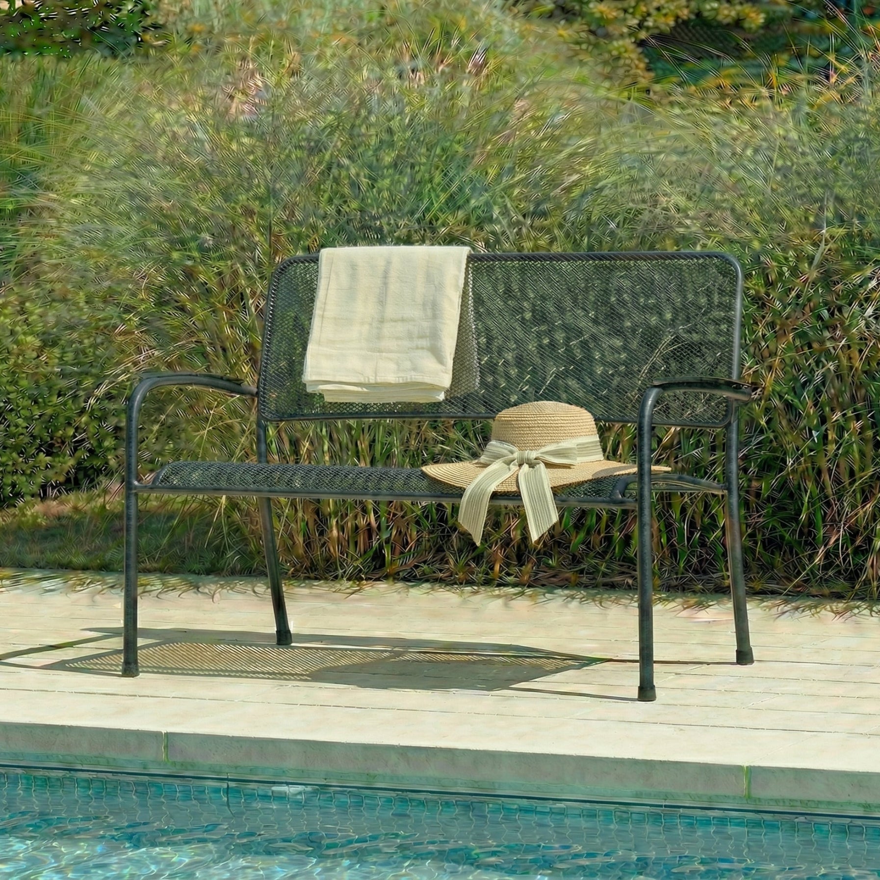 Garden bench with a towel and hat on a wooden deck by a pool