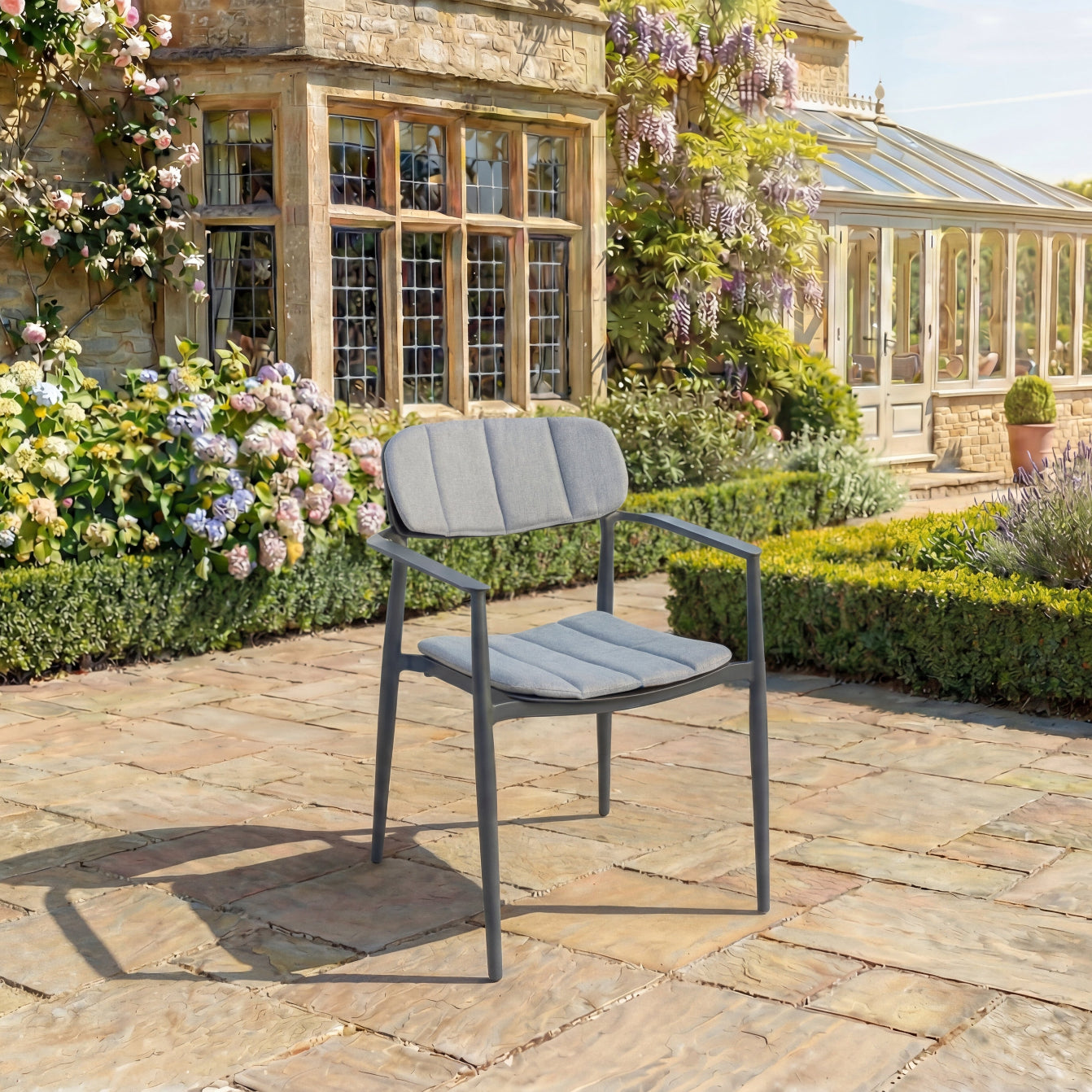 Grey outdoor armchair on a stone patio with a garden and house in the background