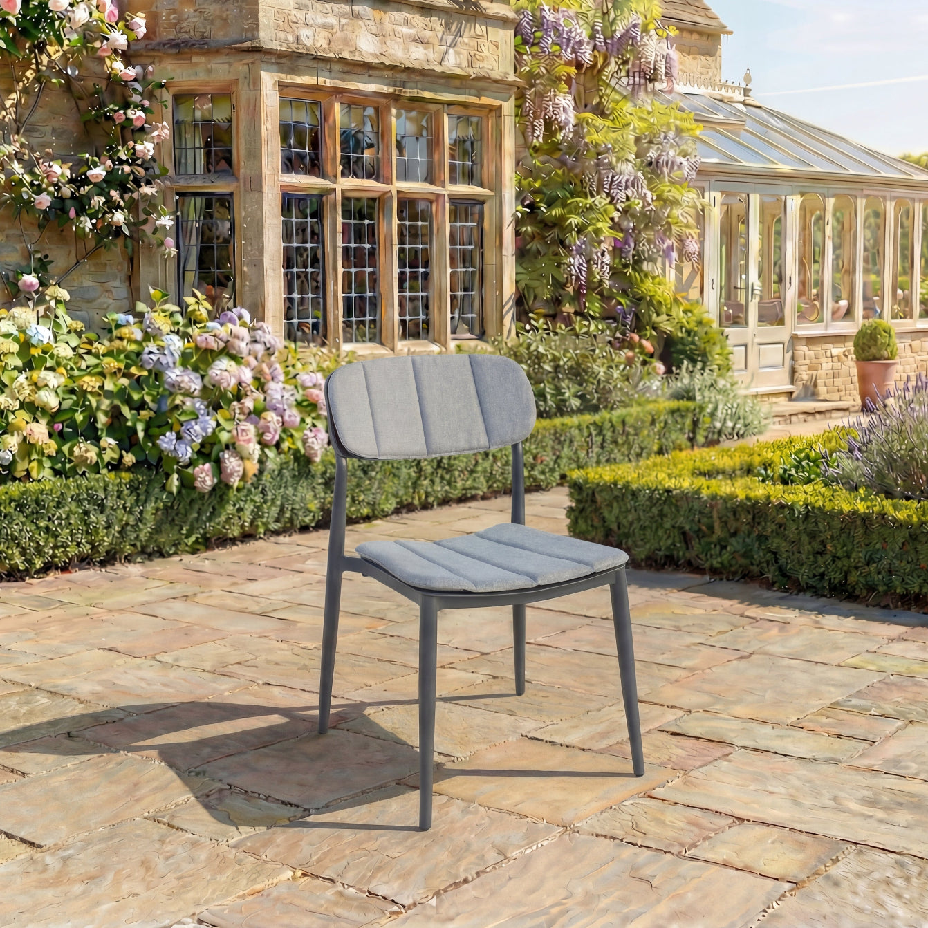Grey outdoor side chair on a stone patio with a garden and building in the background