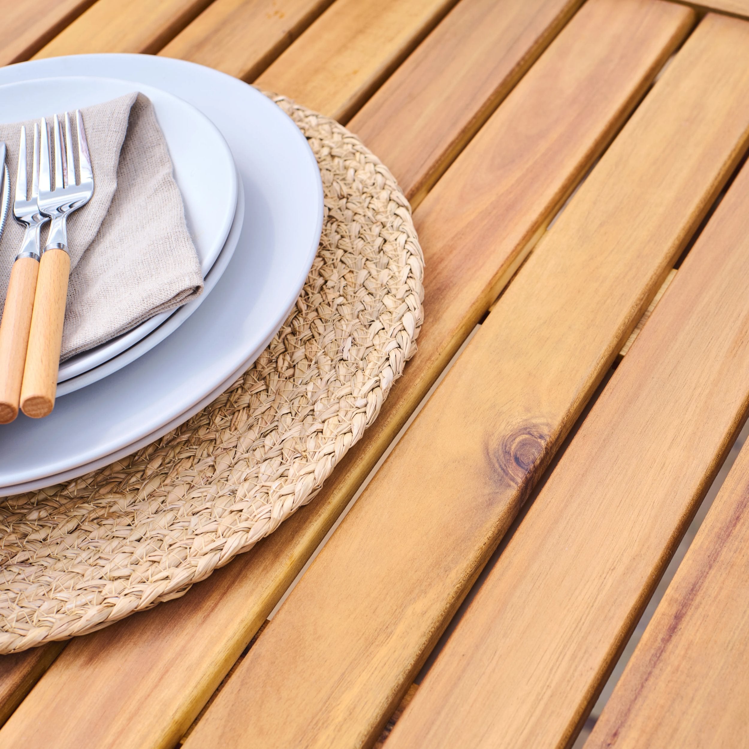 Dinner setting with plates, cutlery, and a woven placemat on a wooden table.