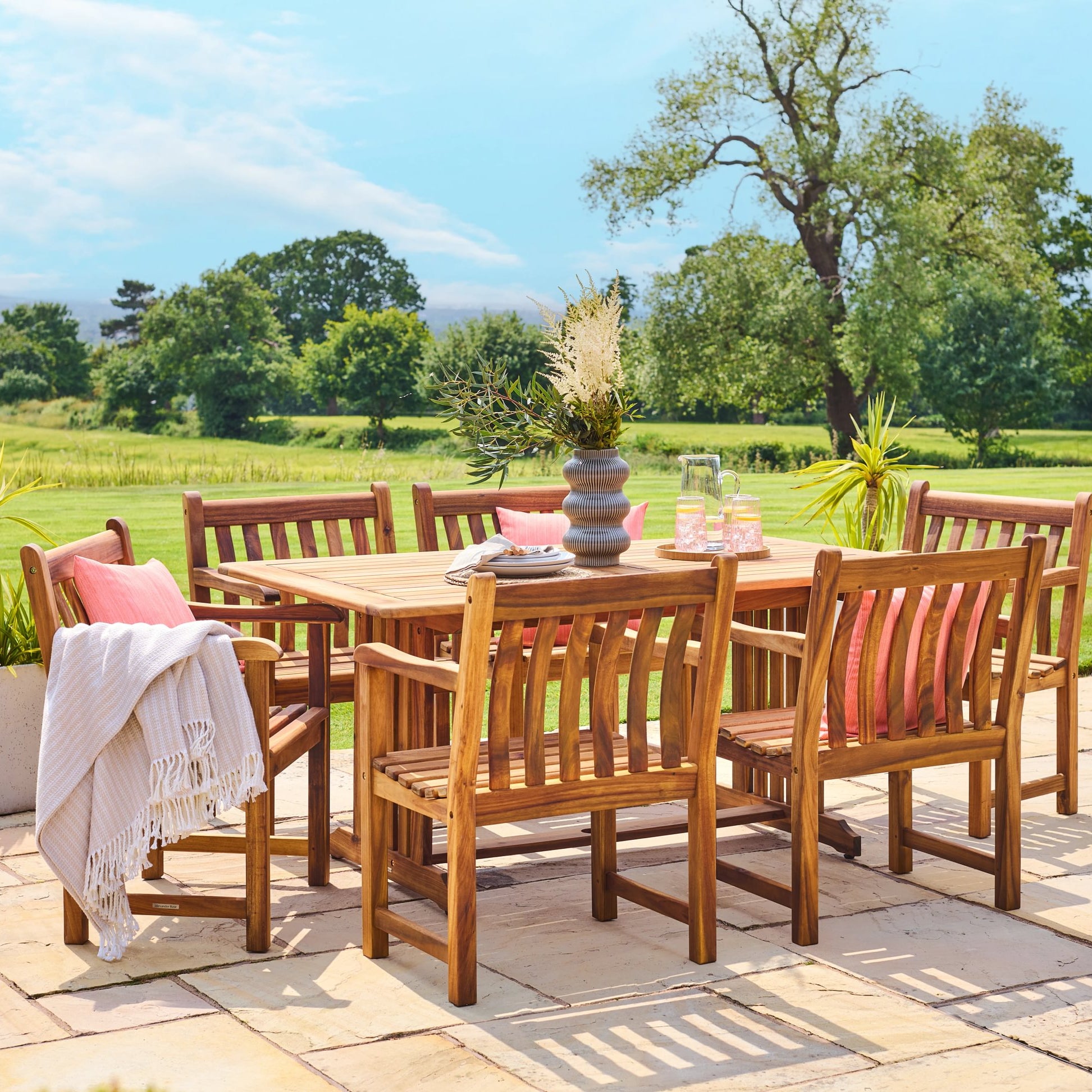 Outdoor dining set with wooden table and chairs on a patio, surrounded by greenery.