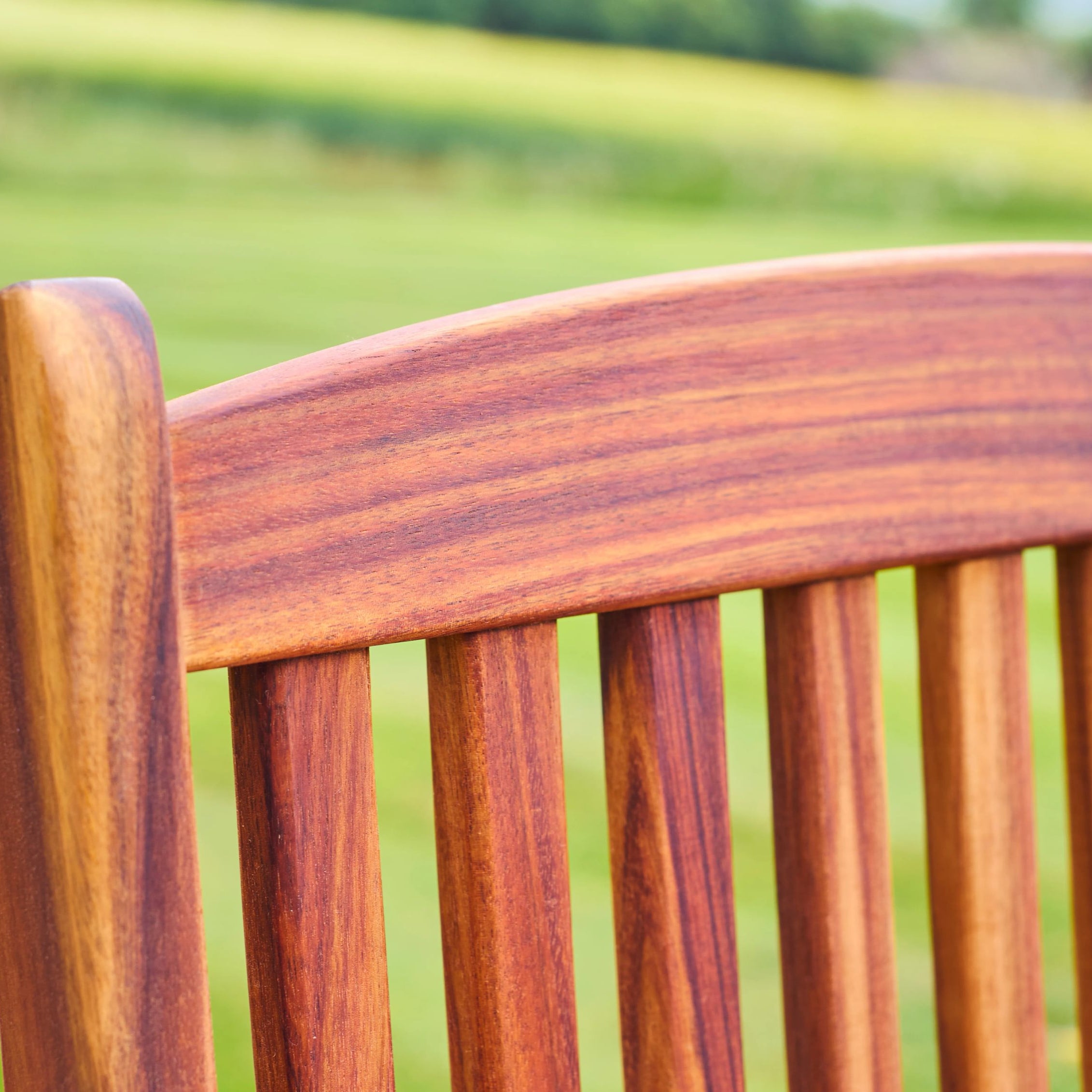 Close-up of a wooden chair with a blurred green field background