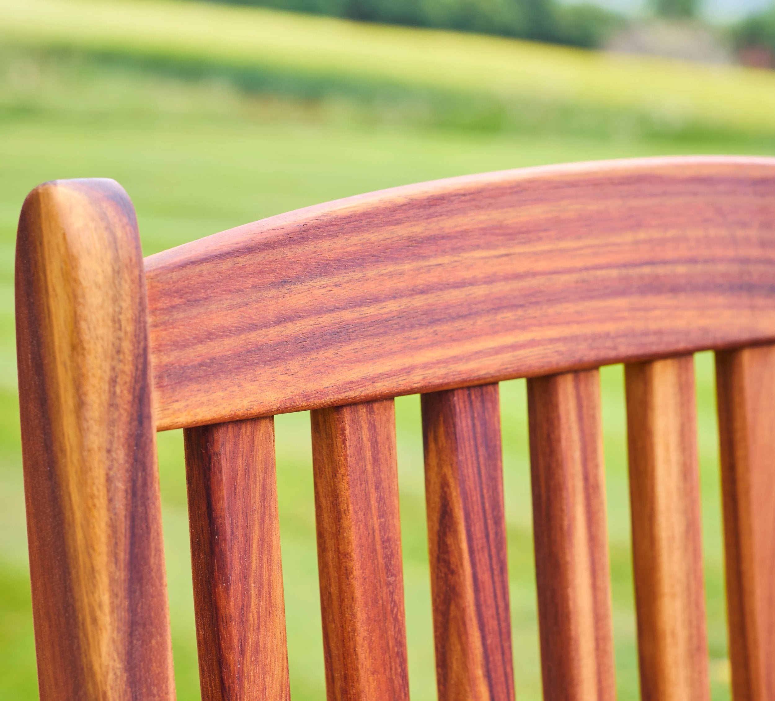 Close-up of a wooden chair with a blurred green field background