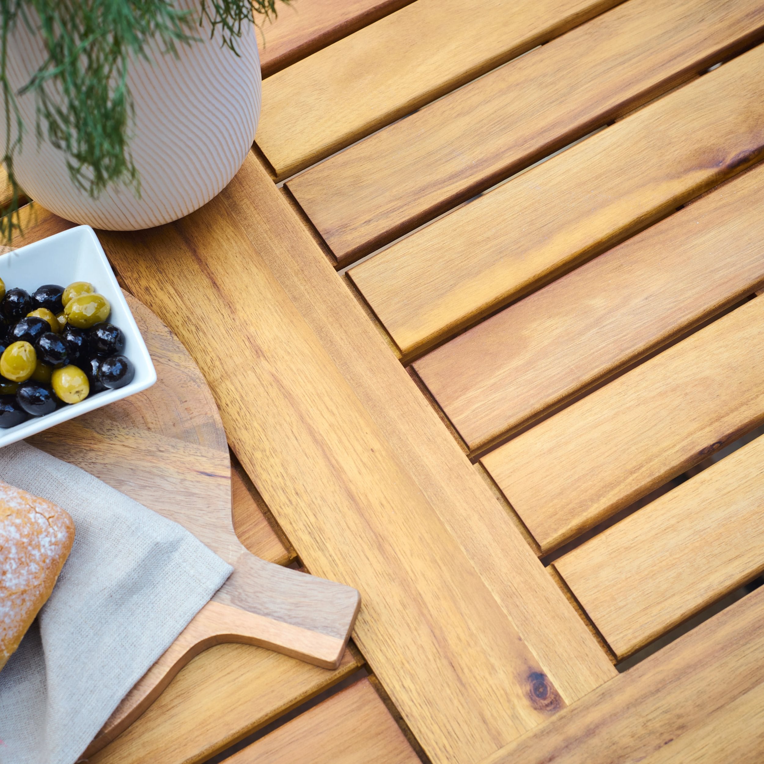 Wooden outdoor table with a bowl of olives, bread, and a plant on a wooden tray
