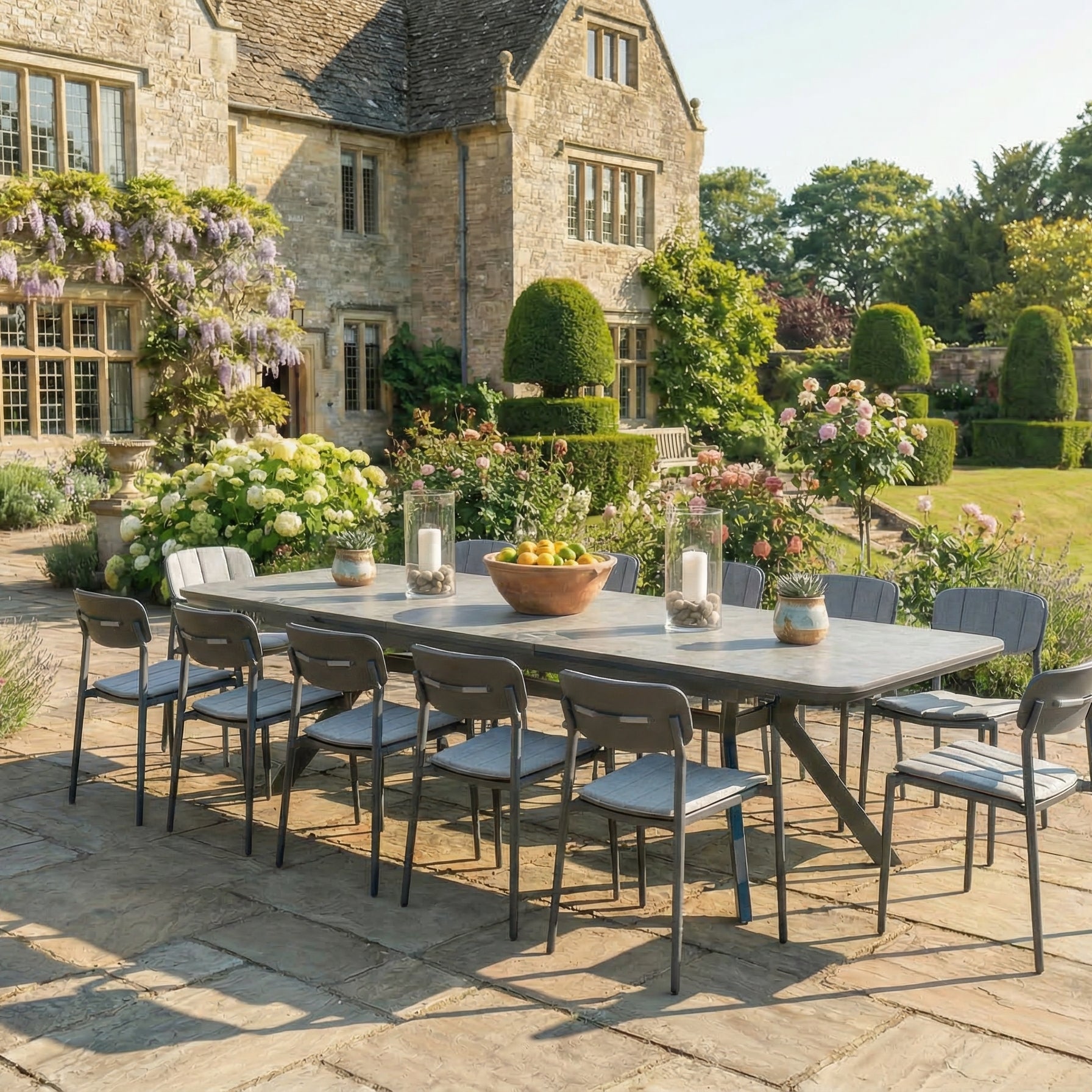 Outdoor dining setup with a large table and chairs on a stone patio in a garden setting.