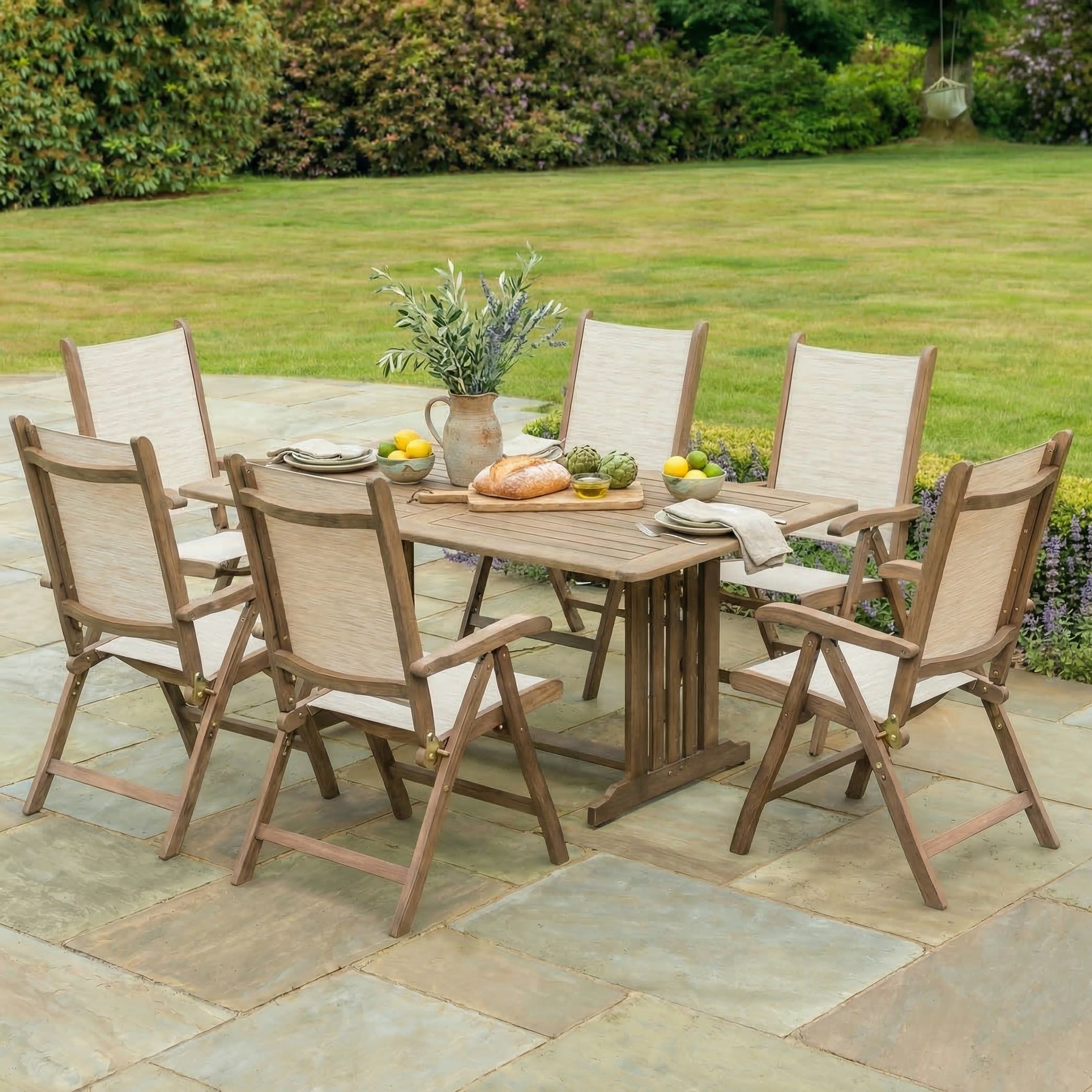 Outdoor dining set with a table and chairs on a stone patio, surrounded by greenery.
