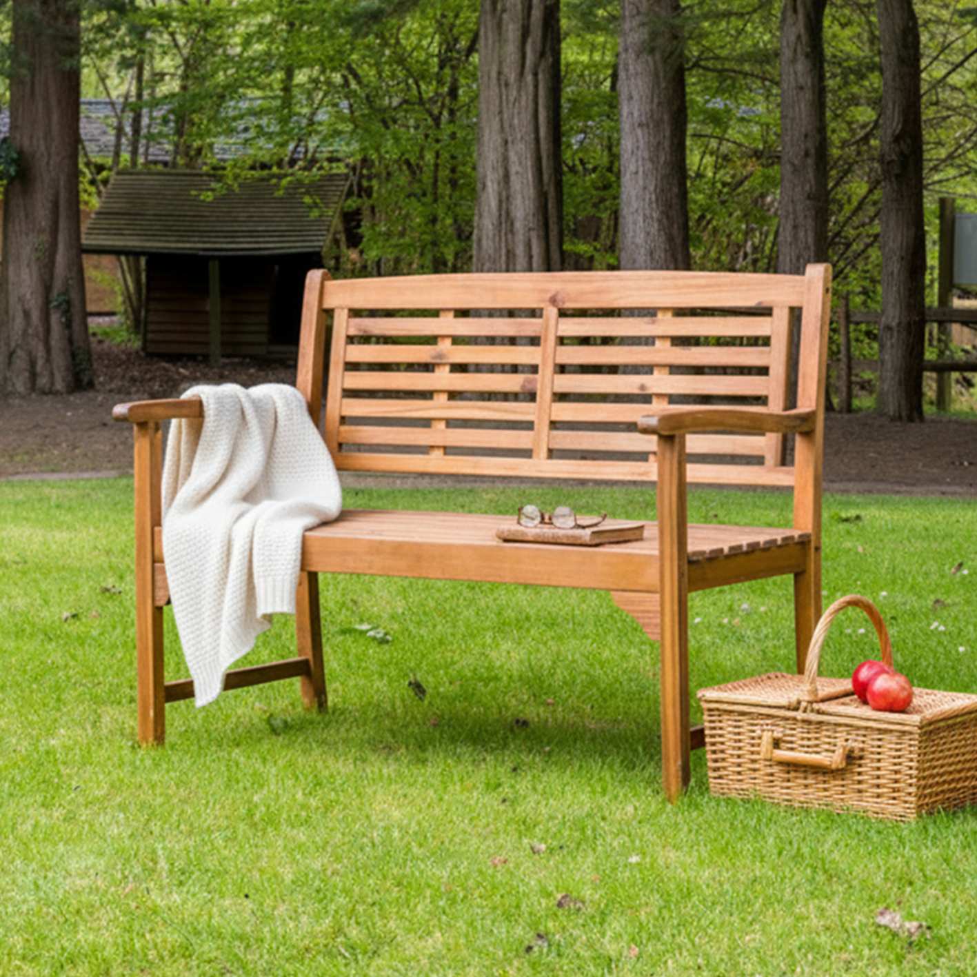 Wooden bench with a picnic basket and apples on a grassy area with trees in the background