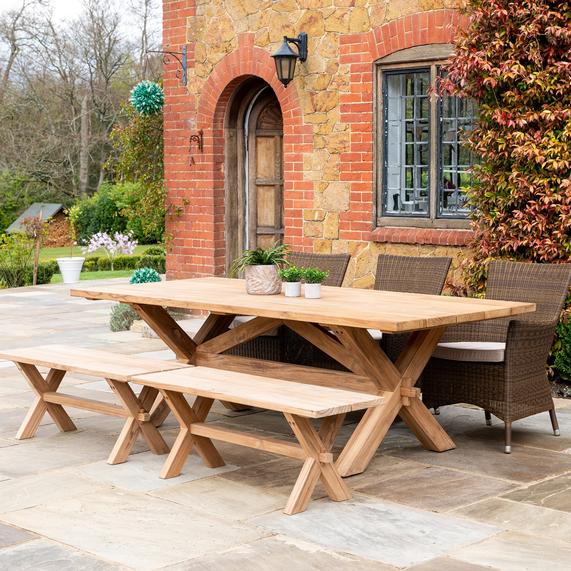 large plank table shown on an outdoor pation with 3 rattan chairs and two plank benches