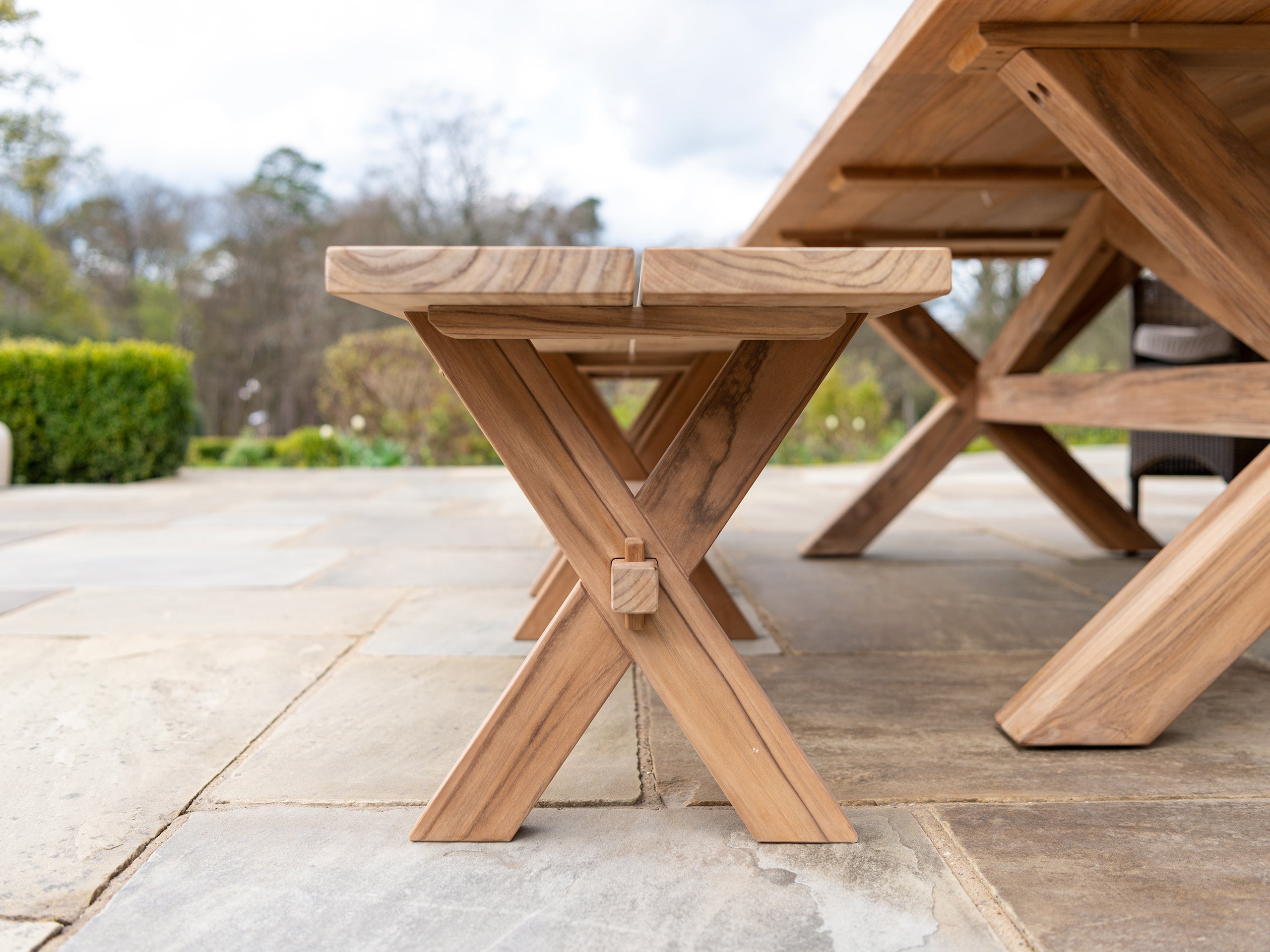 teak plank bench below table on a stone patio