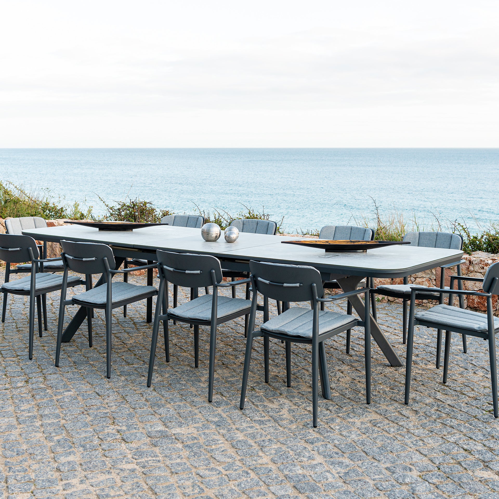 Rimini outdoor extending dining table with chairs on a stone patio by the sea