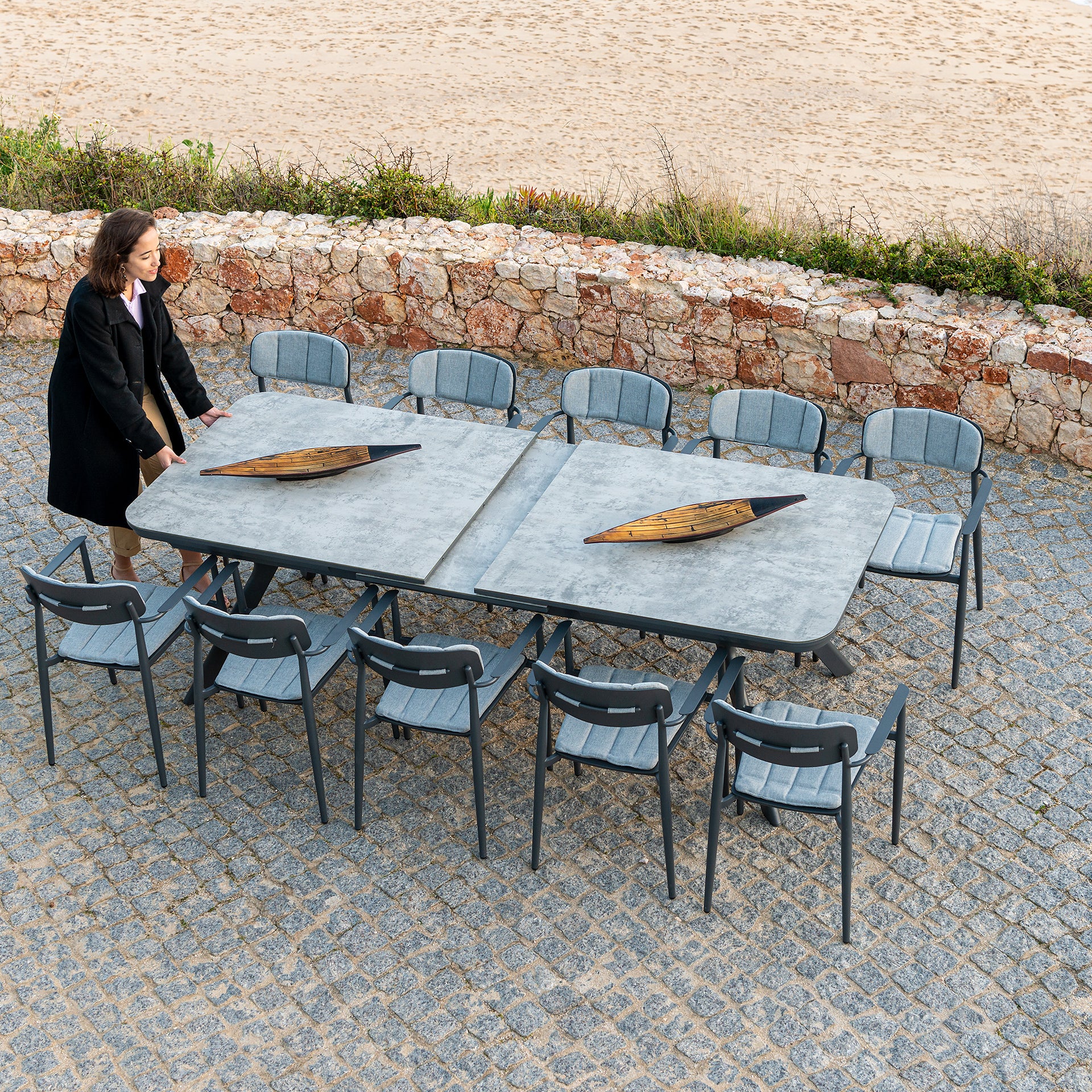woman showing how to easily extend a large outdoor dining table with glass tempered ceramic effect top and 10 matching dining chairs.
