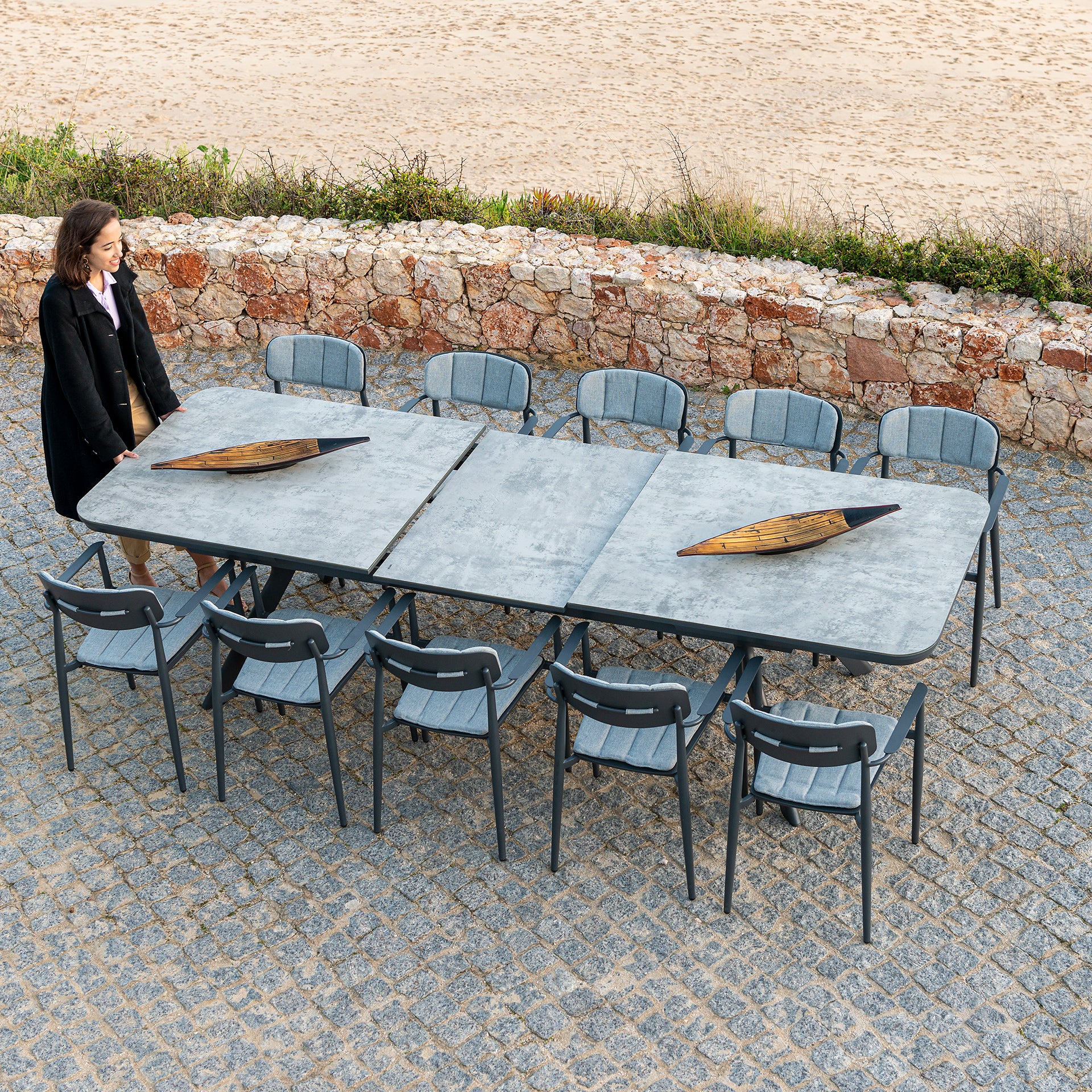 Rimini extending dining table in powder coated aluminium with 10 Rimini chairs on a patio area. The dining table is tempered glass with a grey ceramic effect.