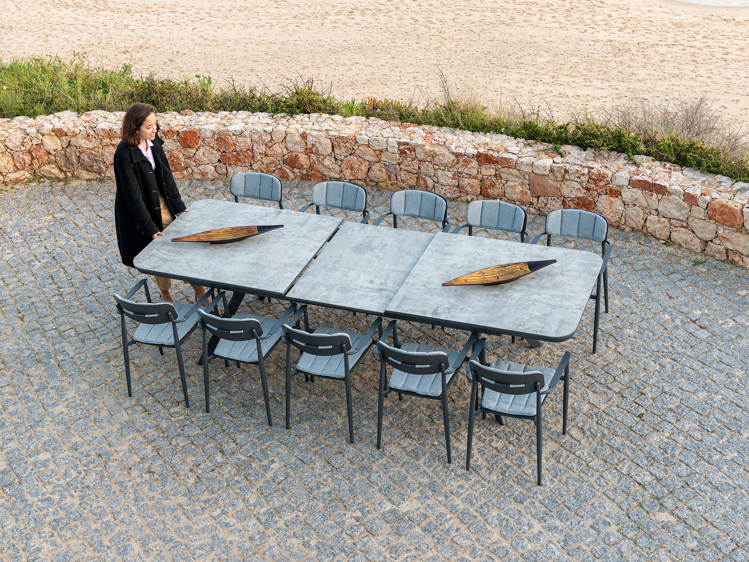 Rimini extending dining table in powder coated aluminium with 10 Rimini chairs on a patio area. The dining table is tempered glass with a grey ceramic effect.